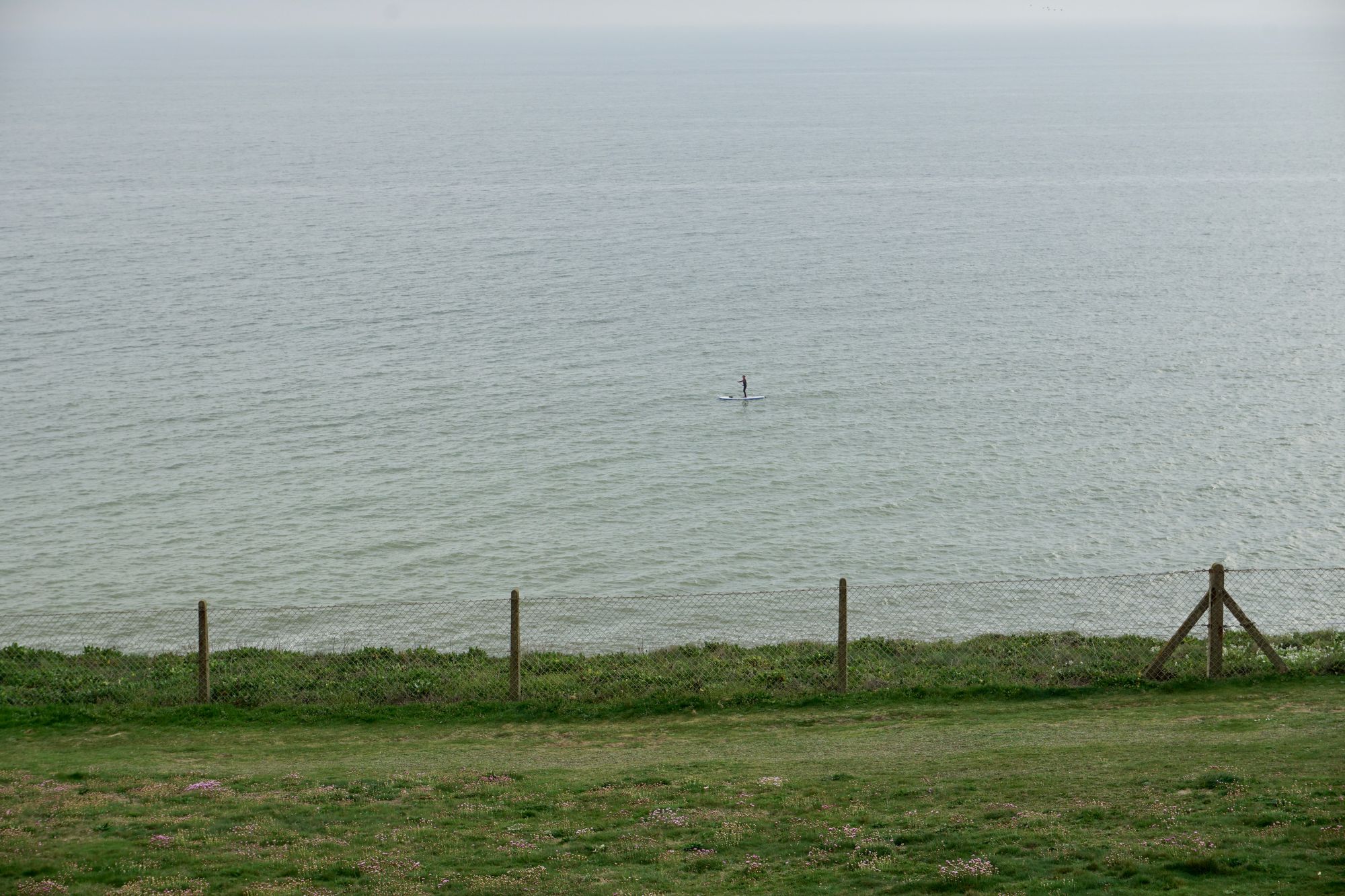 Looking over the edge of the cliff towards the sea. A paddleboarder is visible a good distance out to sea.