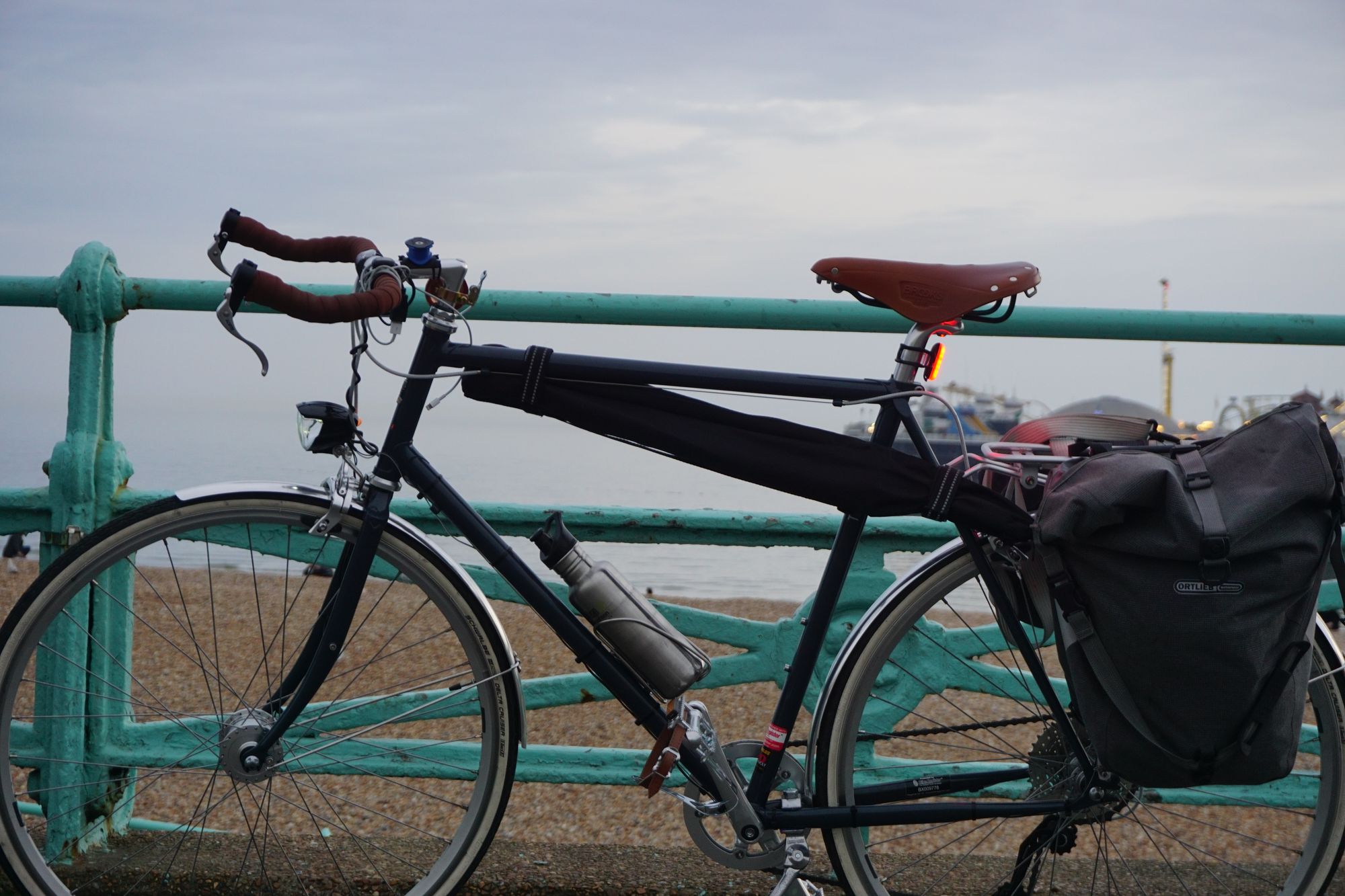 My bicycle against some railings in Brighton. The front light is on. A battery light is turned on and strapped to the seatpost.