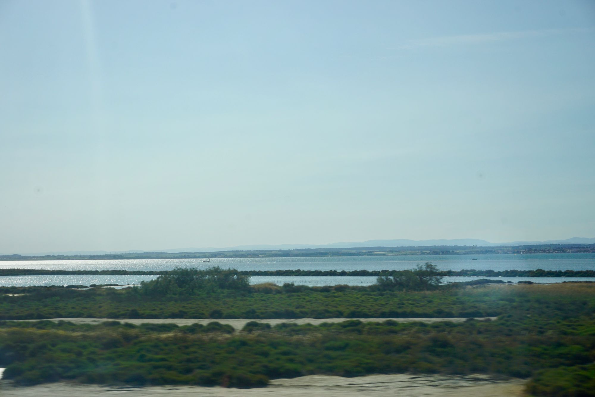 From a train window: Scrublands in the foreground, behind which lies a blue lagoon