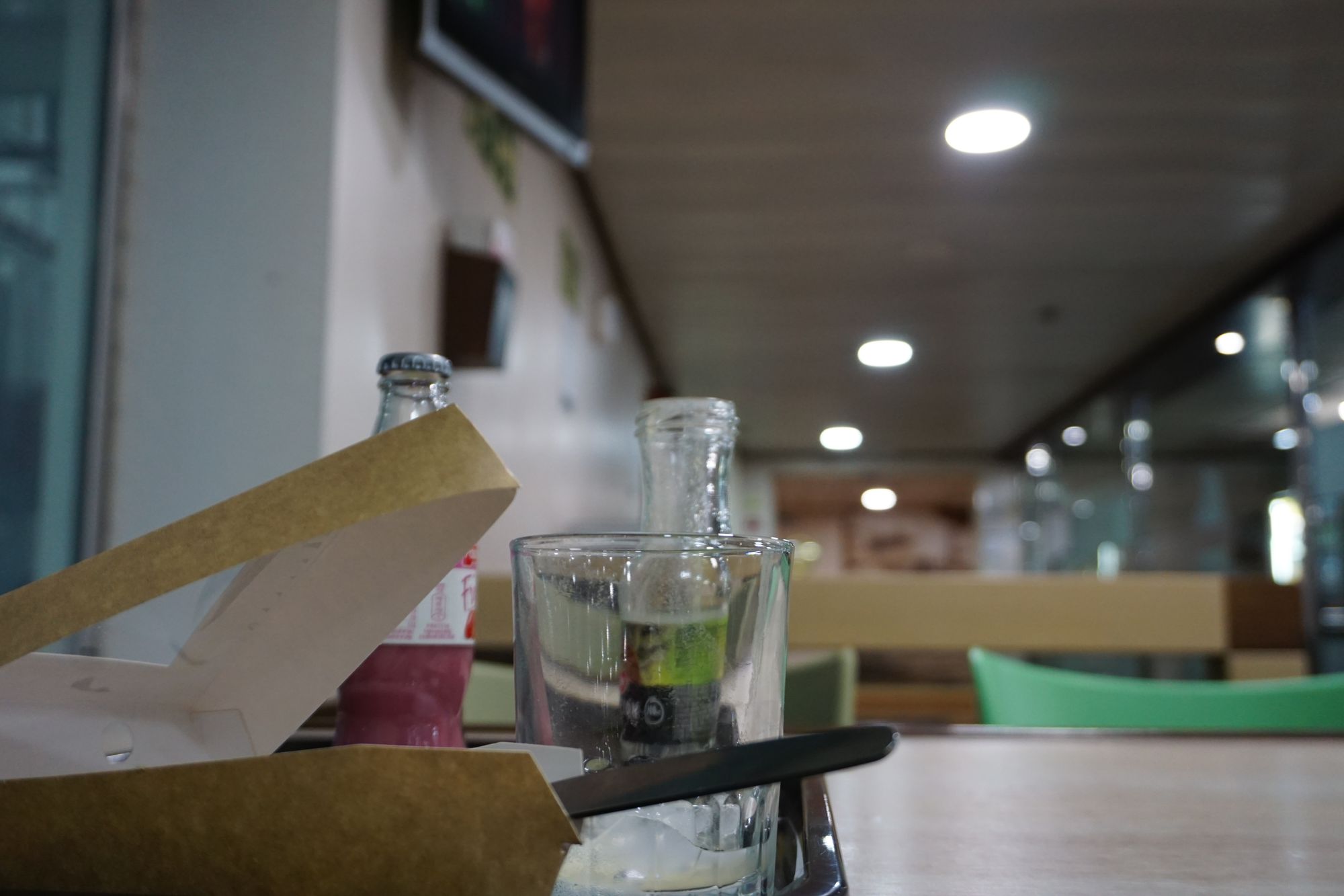 Glasses, bottles, and plastic food packaging on a table in a café like setting.
