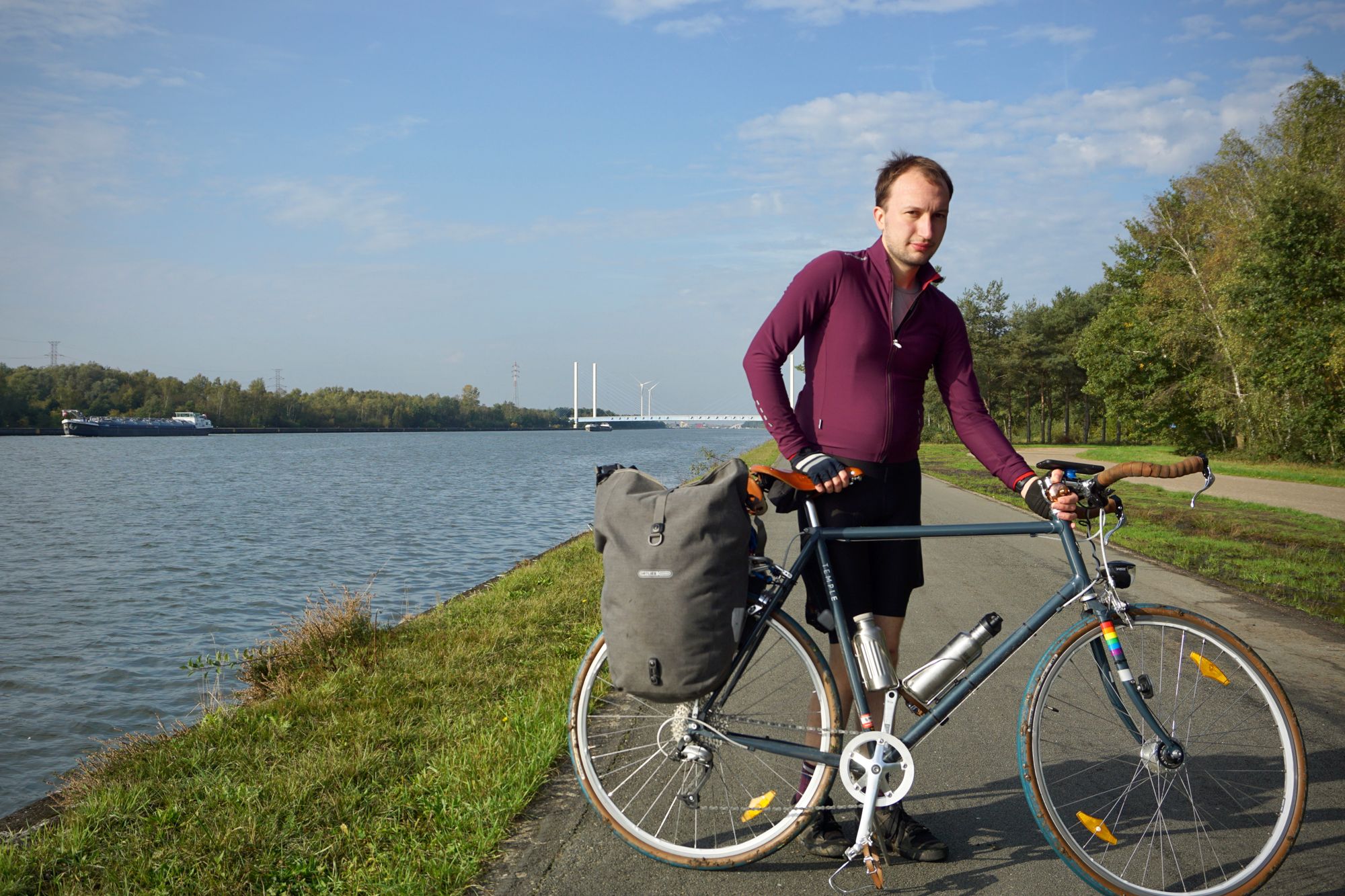 Jonathan stands with his bike on the towpath of a wide canal. The tyres are muddy.