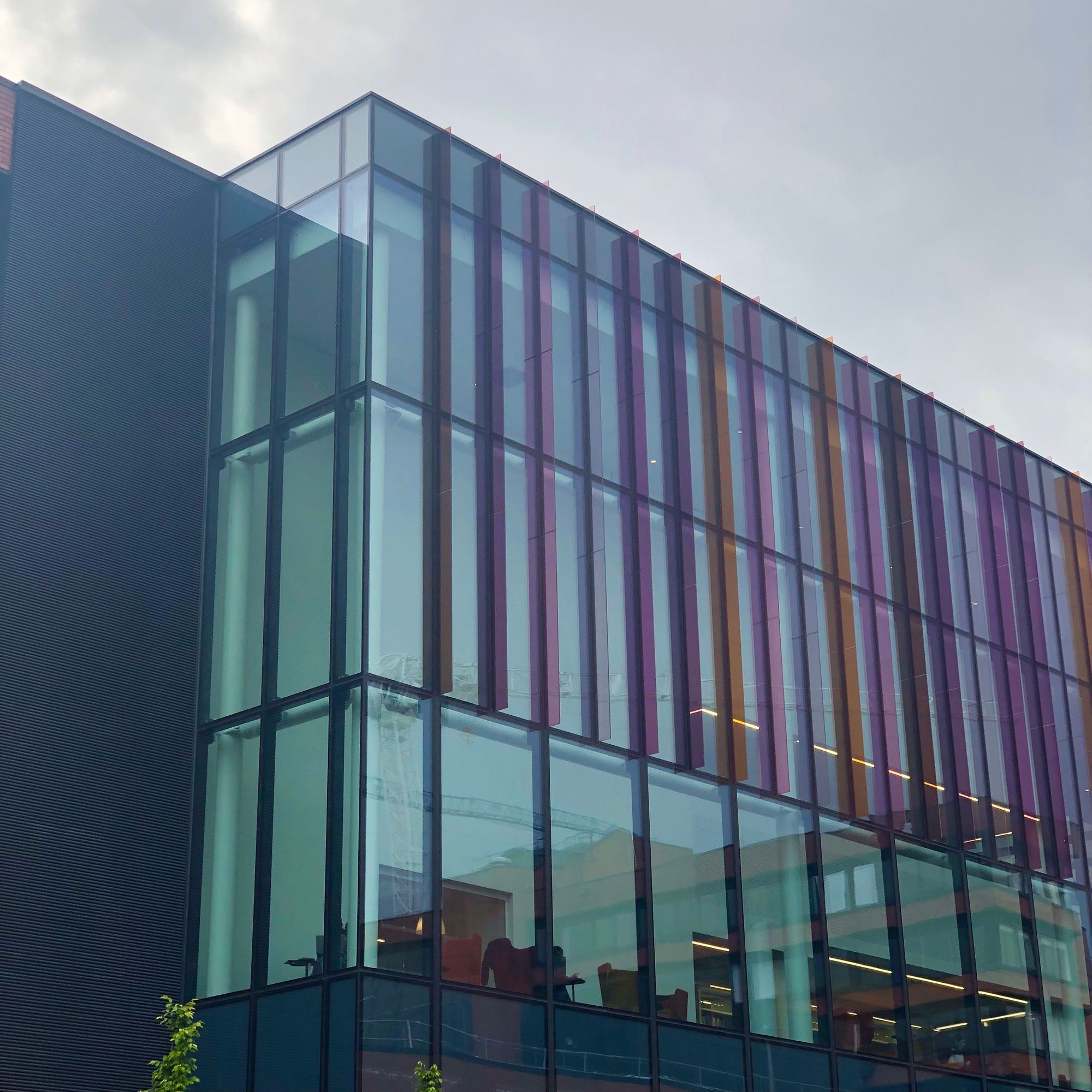 A glass oblong building. Narrow, multi coloured panels of glass jut out perpendicular at regular intervals.