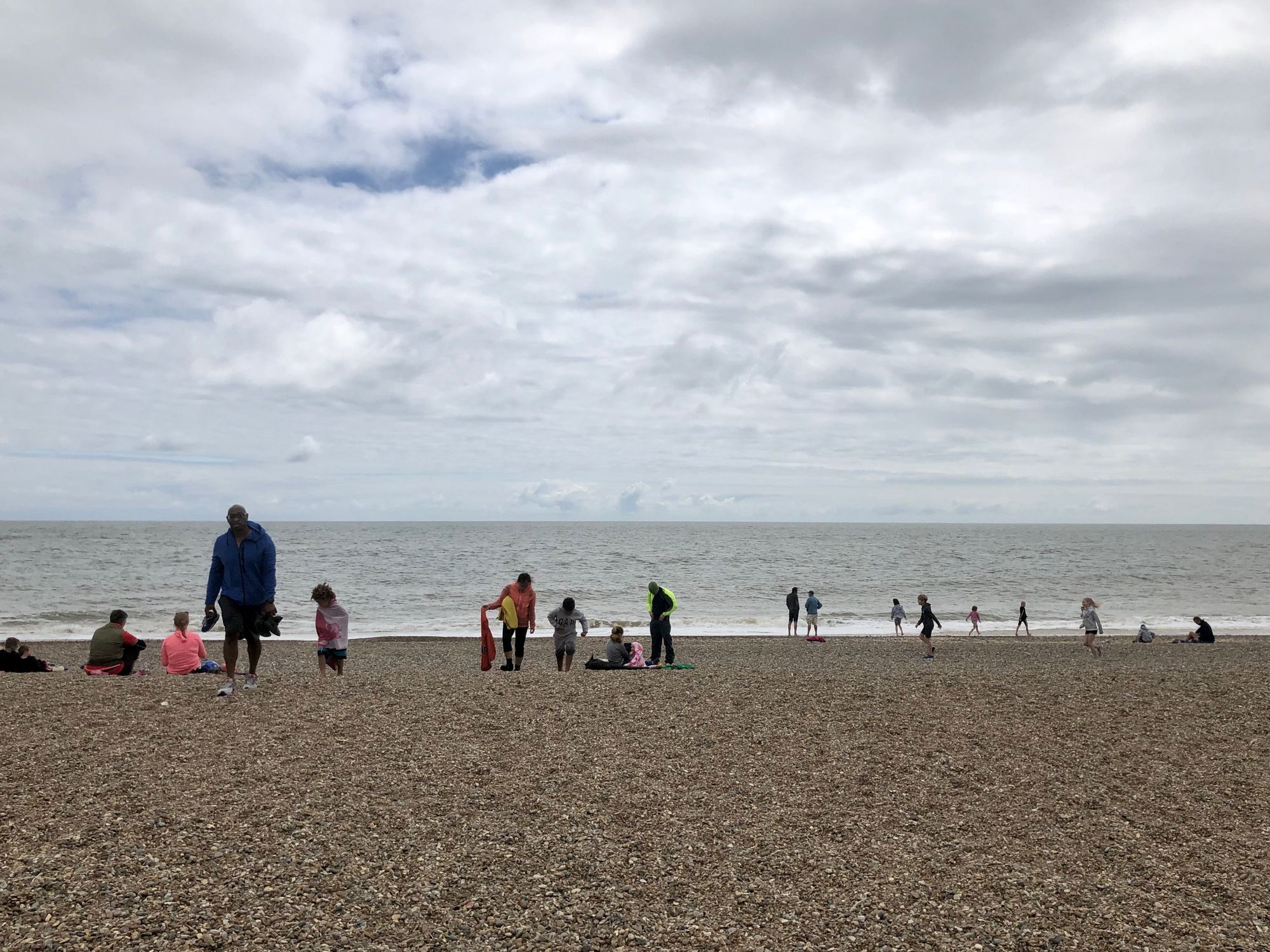 A steep shingle beach with various people standing on it.