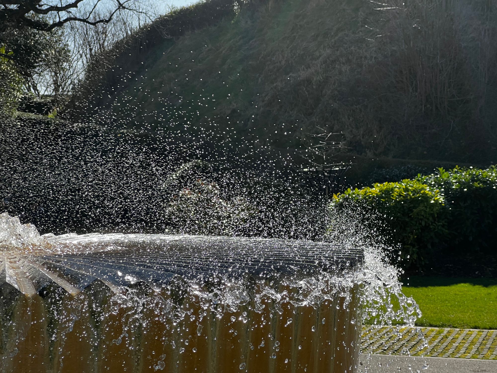 Spray is buffeted away from the surface of a flat fountain with ridges on the surface.