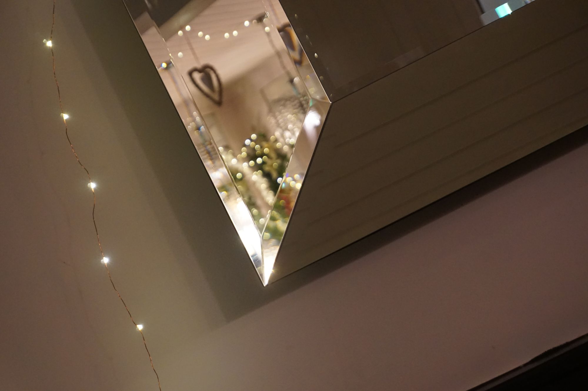 Fairy lights on a wall reflected in a mirror frame, which shows more fairy lights amongst fake hanging plants.