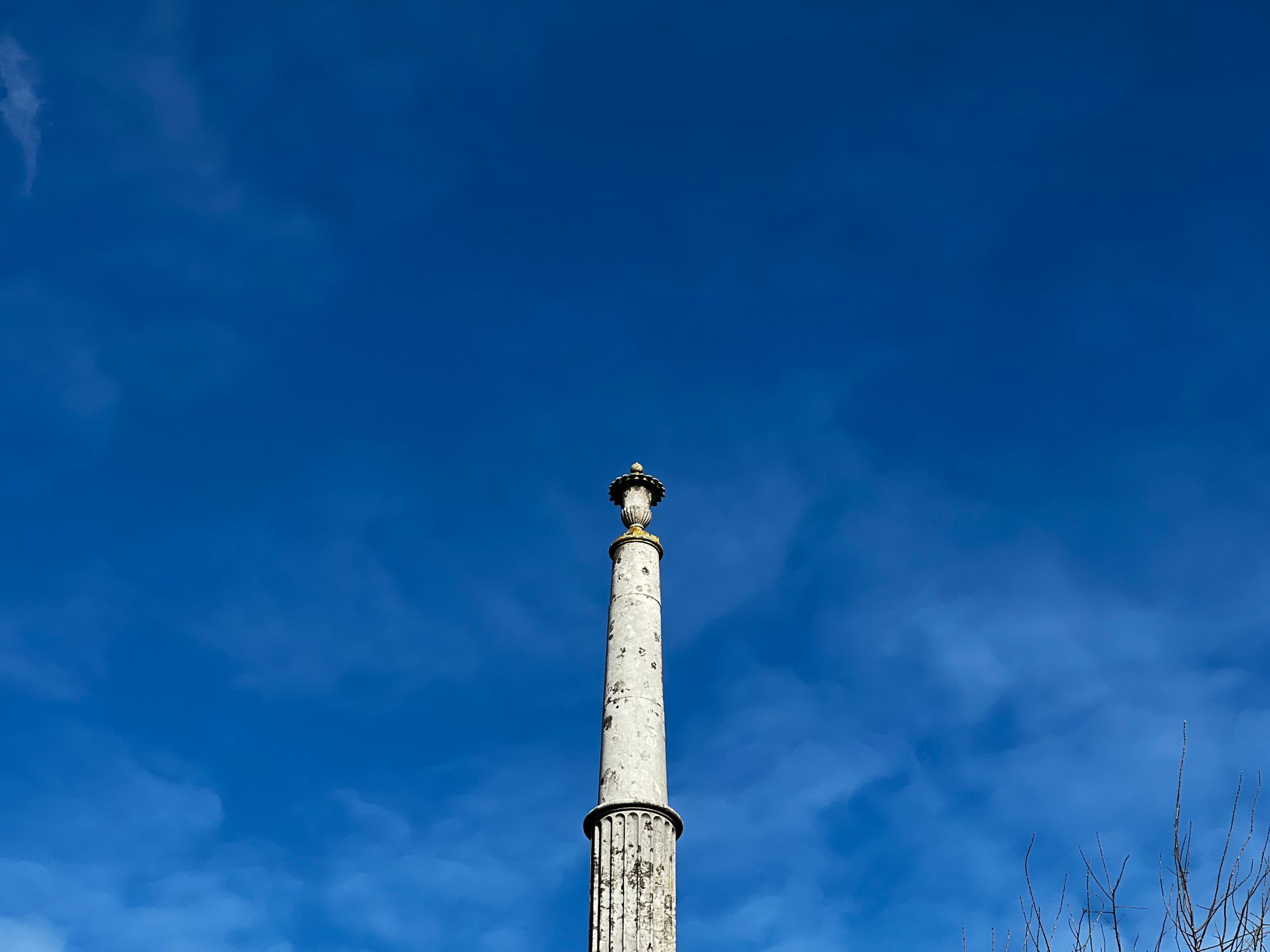 A weathered round stone obelisk with a gourd-like feature on the top, on a clear day.
