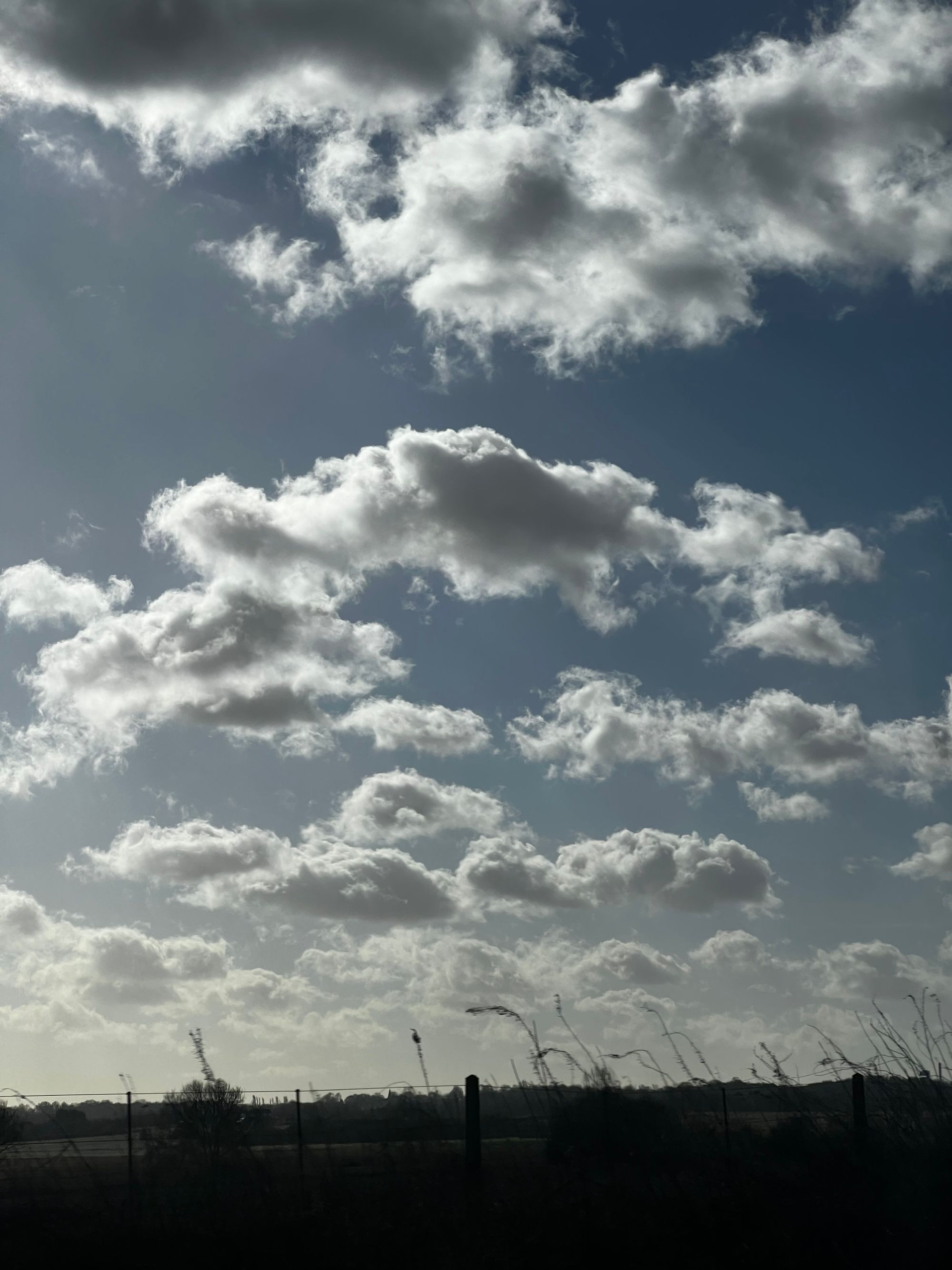 View from a tinted train window of some fluffy clouds and silhouetted scenery moving past.