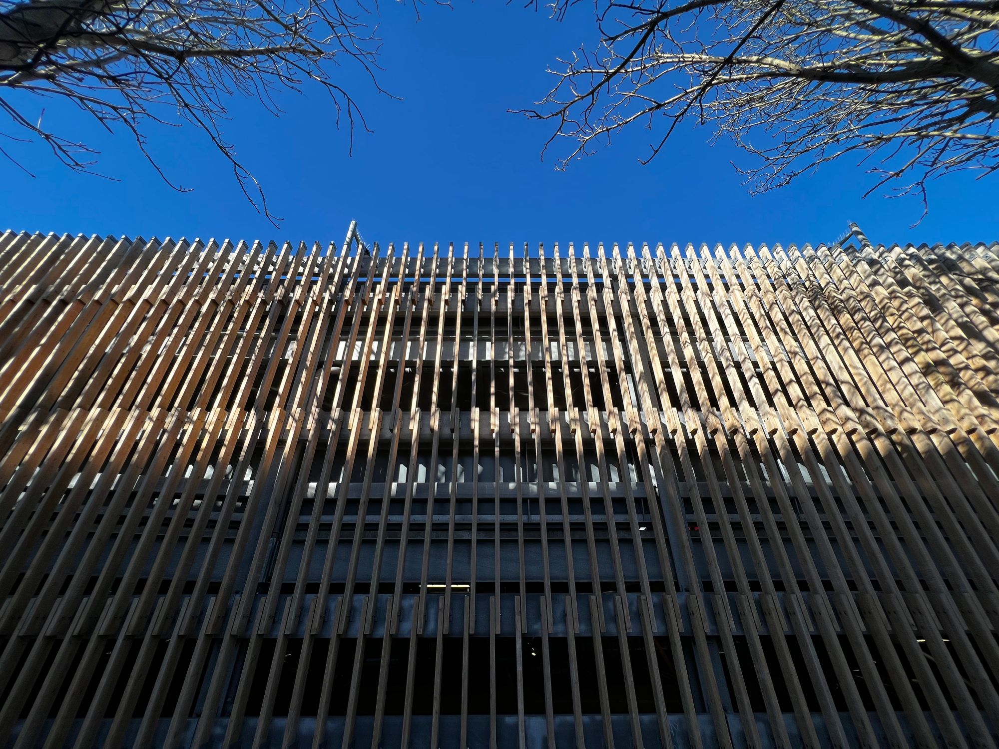 An imposing multi-storey car park with pale wooden planks perpendicular to the building edge forming the cladding.