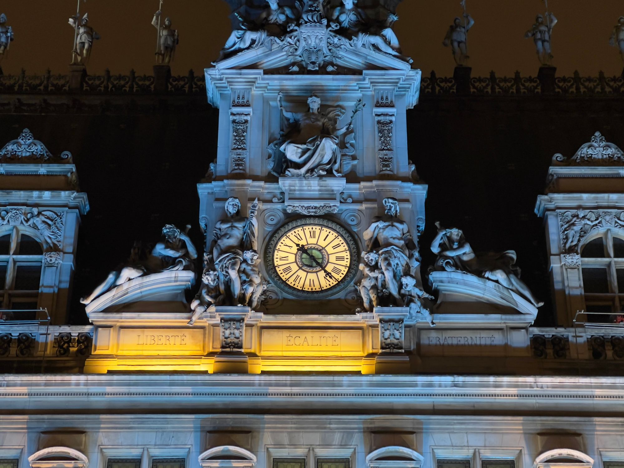 The clock frontage of Hôtel de Ville showing about 10pm. The “Liberté” and “Égalité” panels are lit, “Fraternité” is not.
