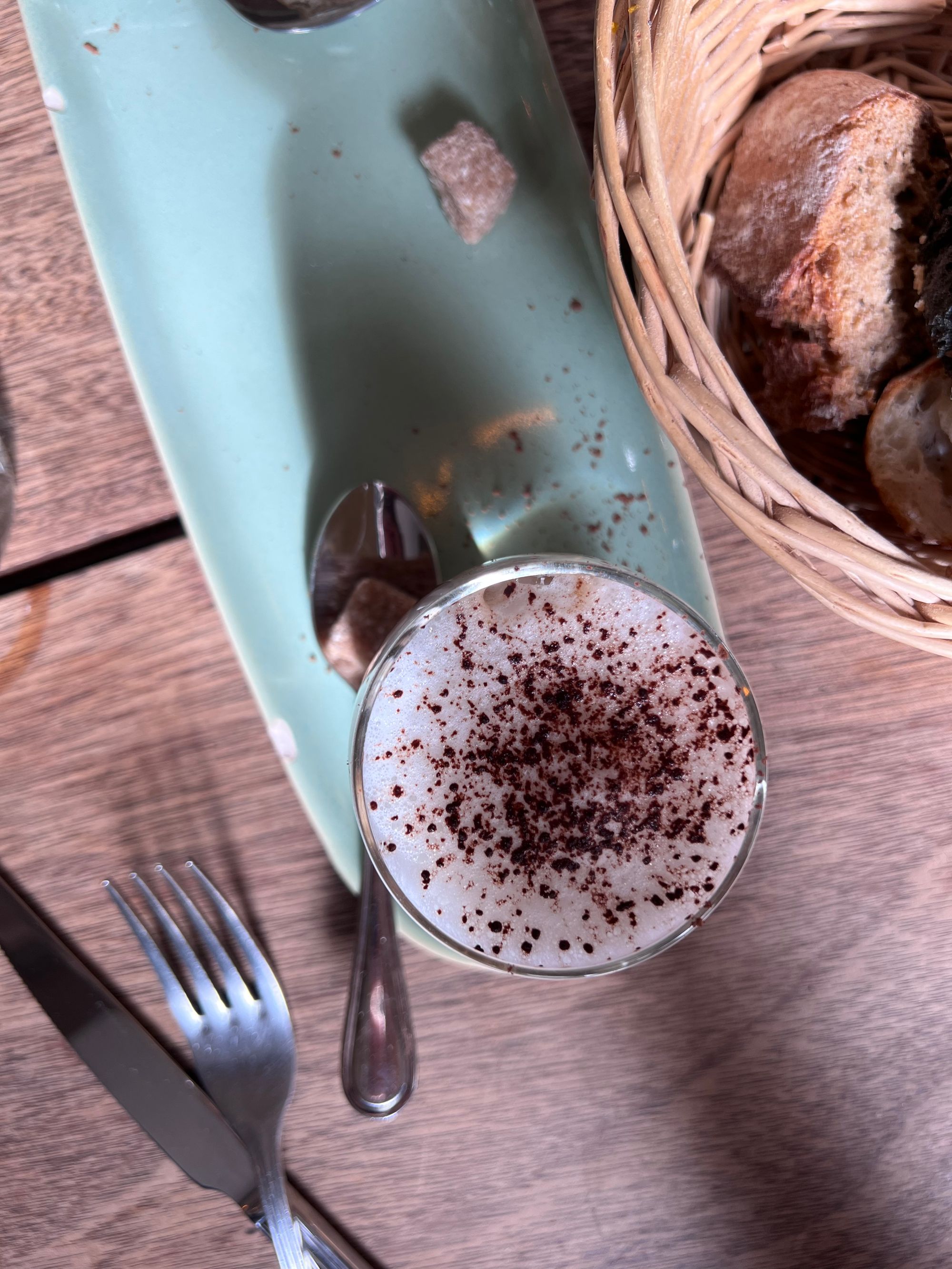 A glass of coffee on a serving plate with sprinkles of chocolate on the foam.