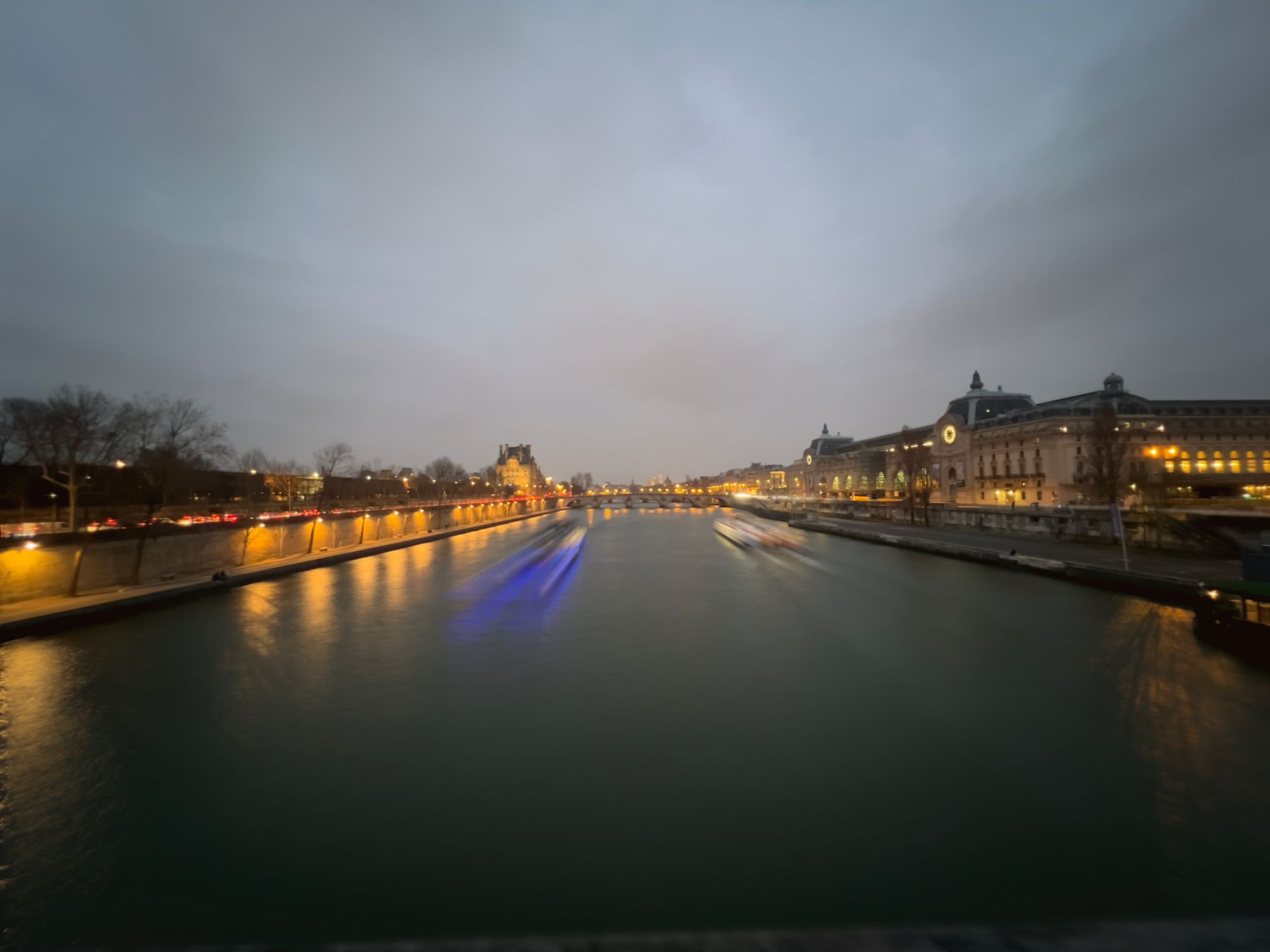 The Seine at dusk from a bridge looking towards Musée d’Orsay. Boats passing make pretty light trails.