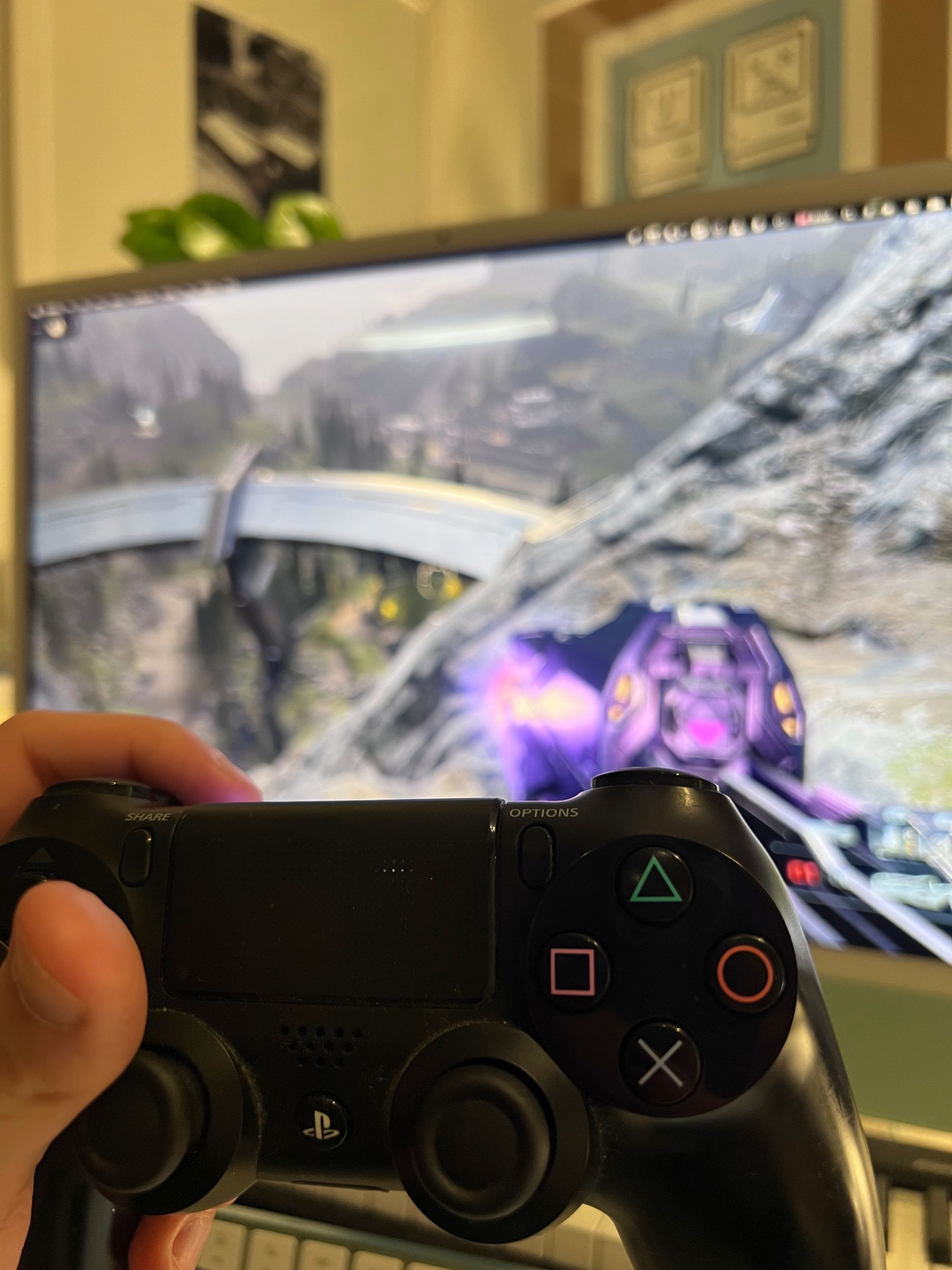A hand holding a PlayStation 4 controller in front of a green 2021 iMac playing Halo inside a browser.
