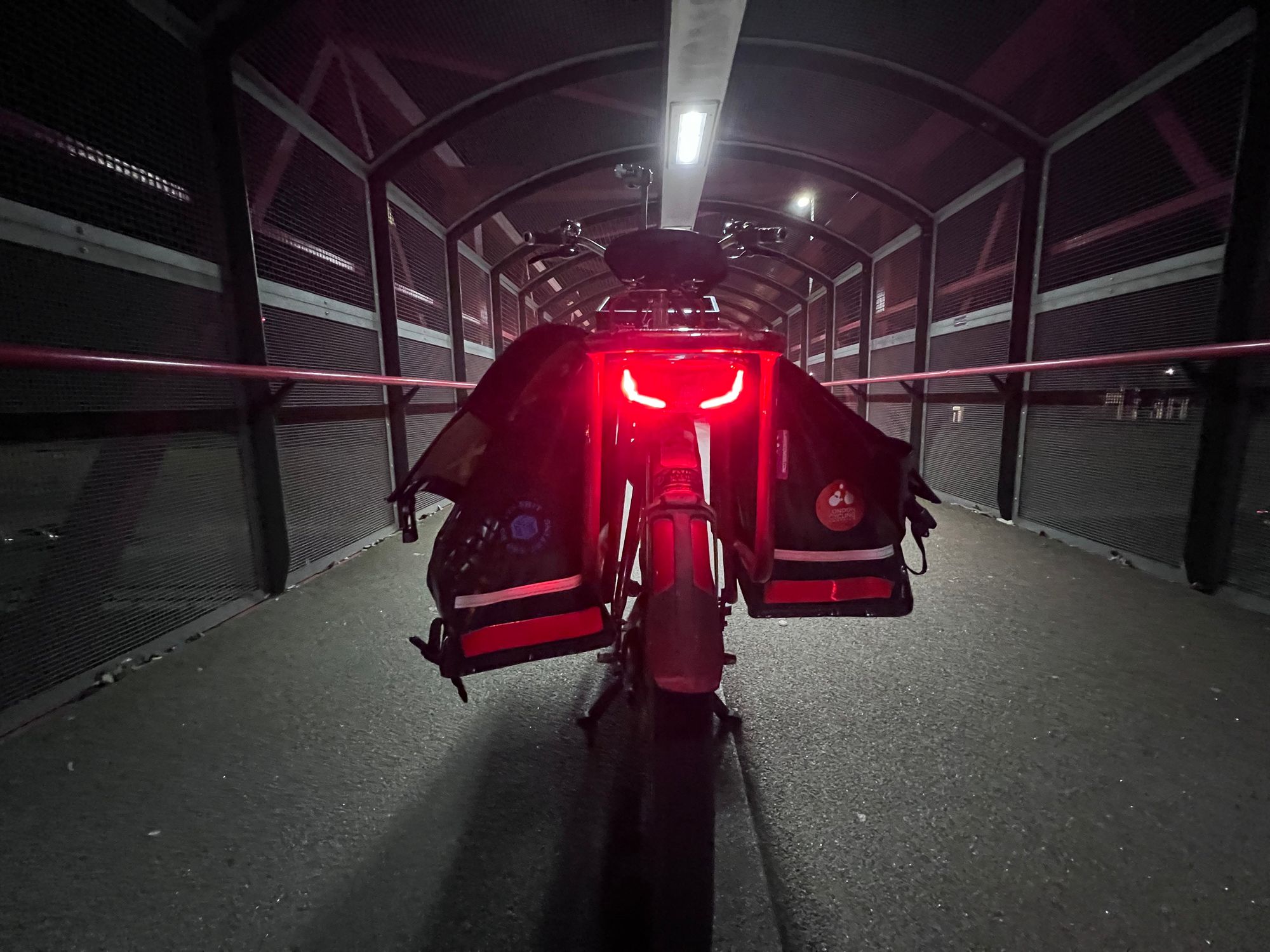 The rear rack of a big red bicycle with its tail light on, showing two curved downward arcs that look like a set of evil eyes.