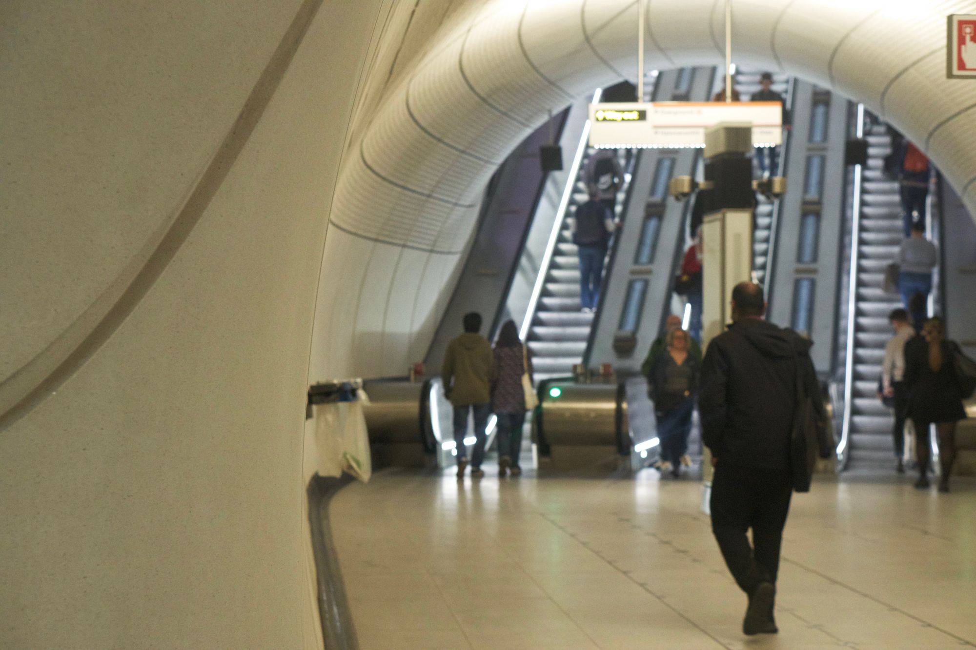 An escalator seems to rise through a curved tunnel from a landing. The walls bend and have no right angles.