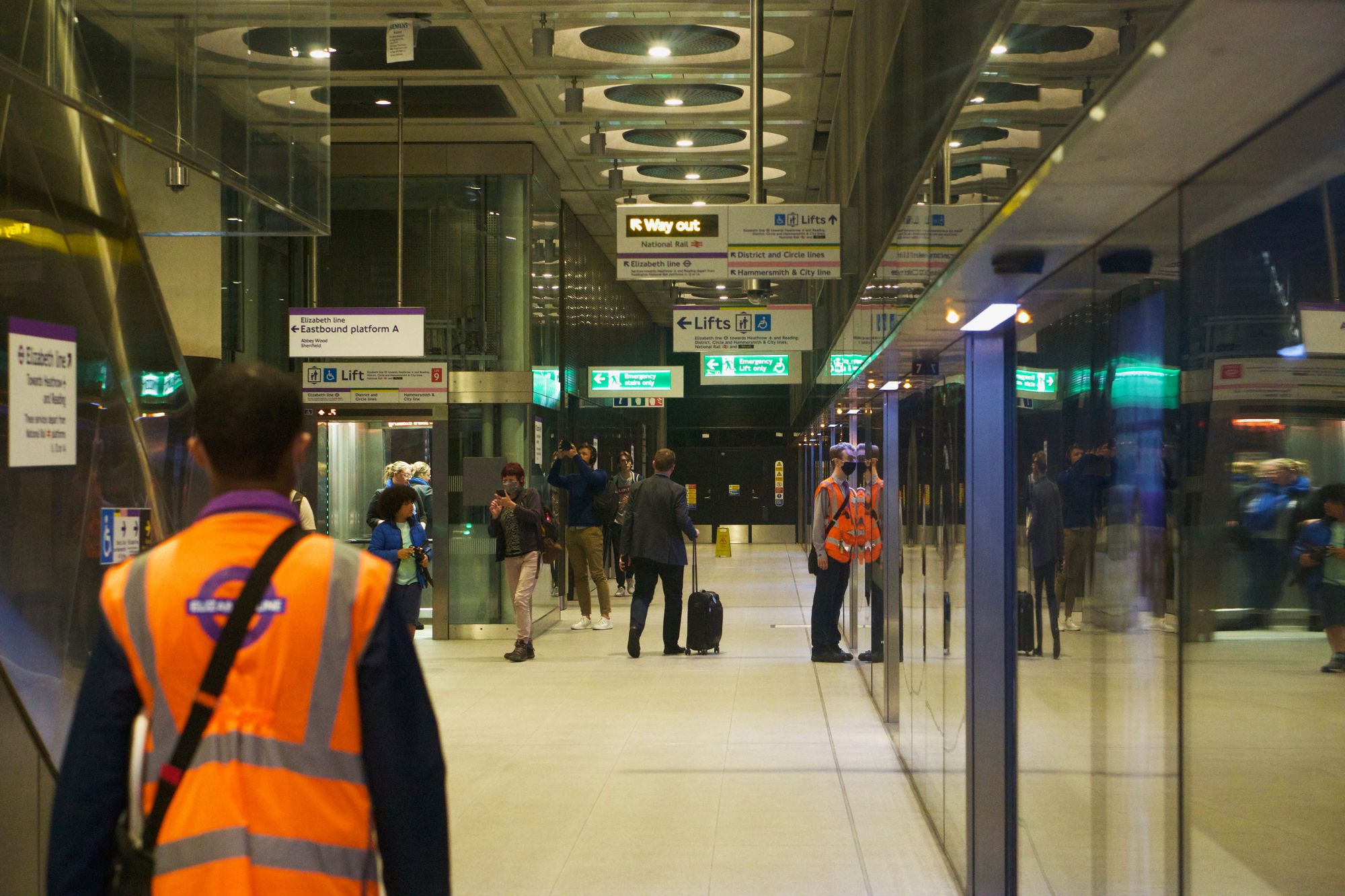 The Elizabeth Line platform at Paddington, with people getting into a lift. A platform assistant pokes his head inside the doors to check inside a terminating train.