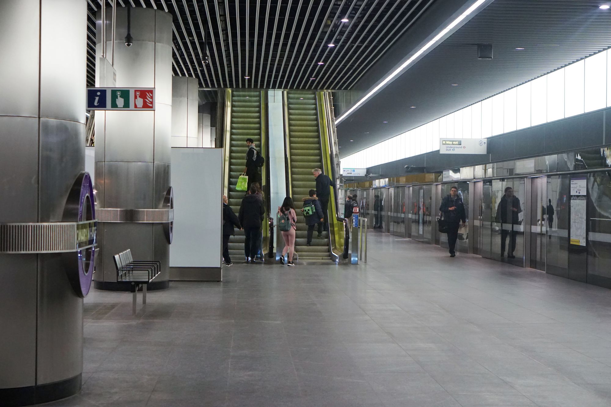 Canary Wharf Crossrail station platform, with edge doors and a pair of escalators with yellow acrylic bannisters leading up.