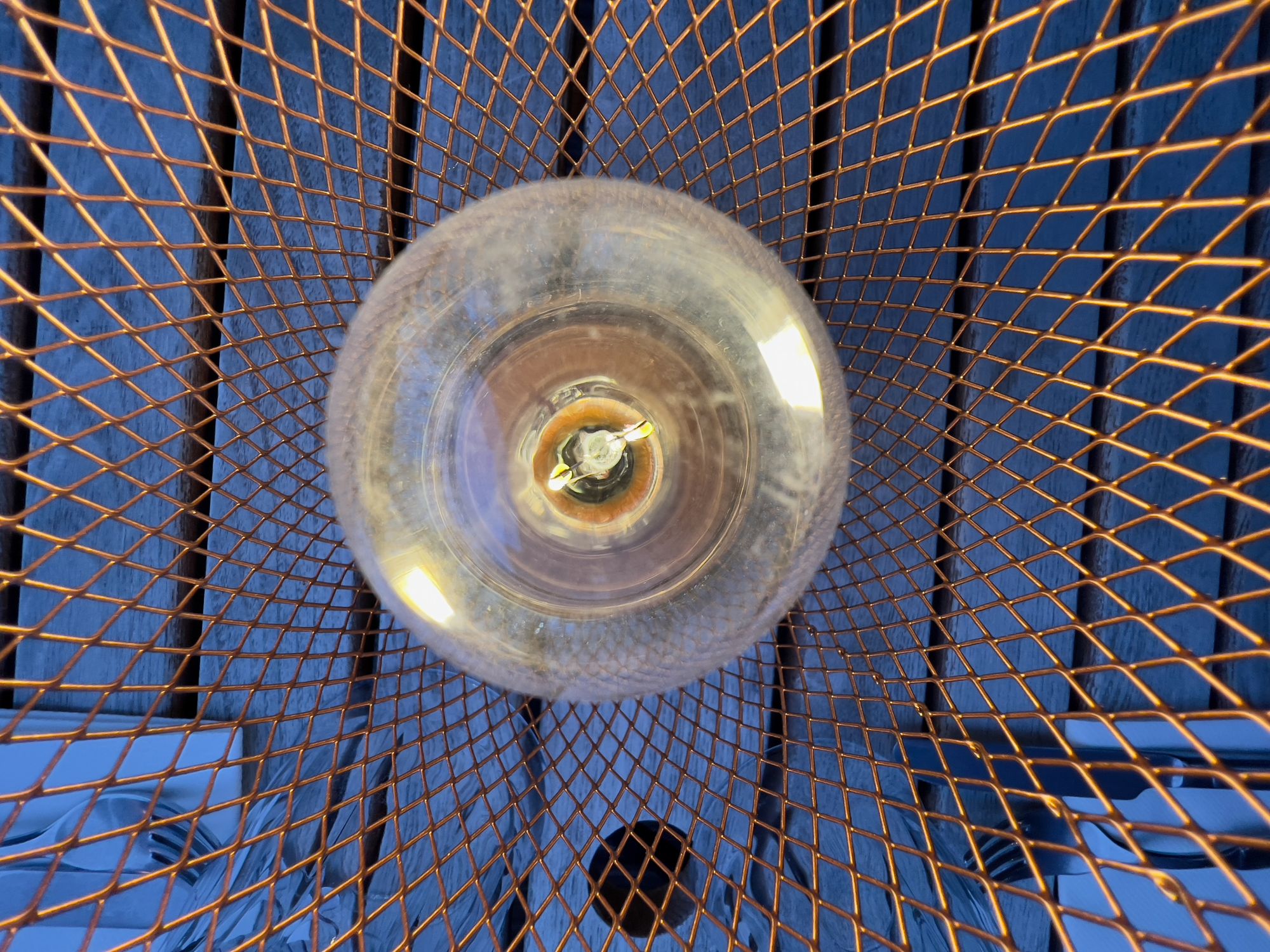 Detail of the top of a lit light bulb in a copper lattice lantern on a wooden table.
