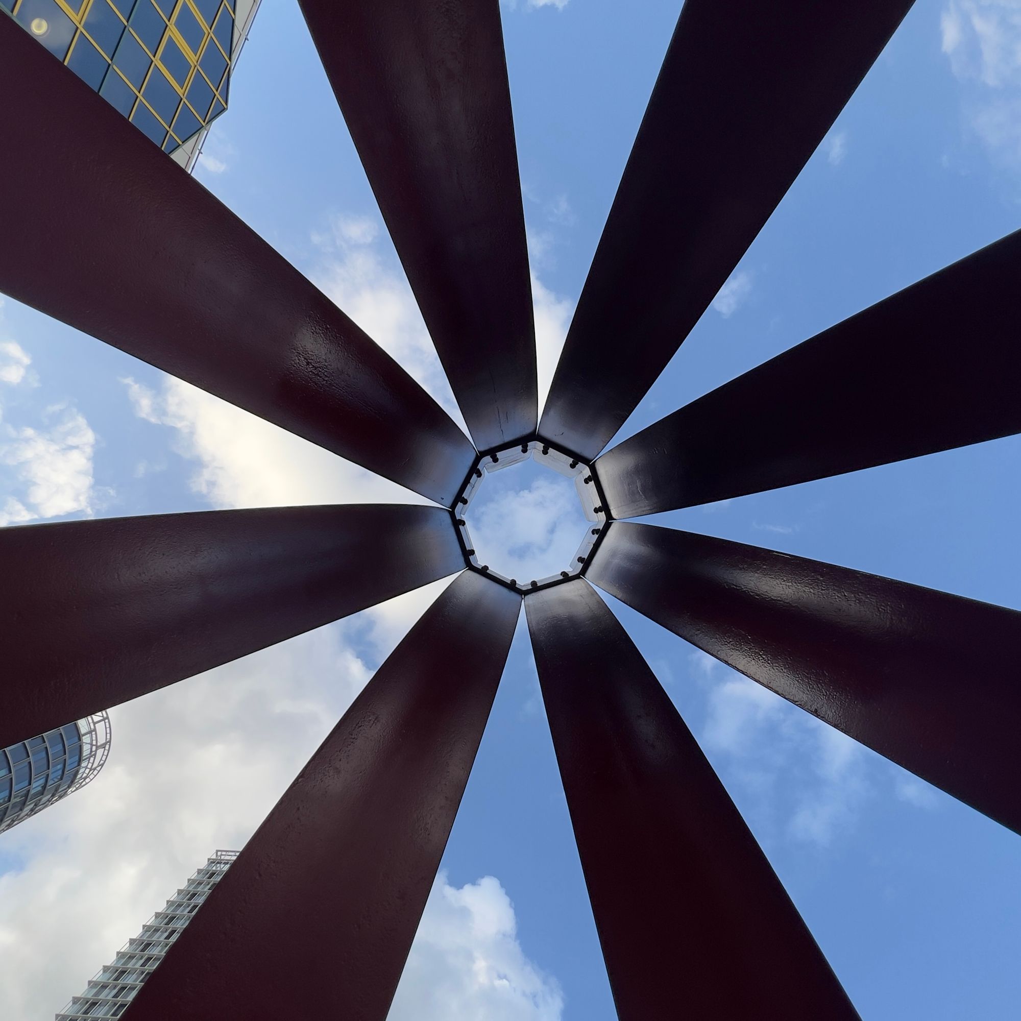 Looking up into a blue, cloudy sky, through the centre of eight rails rising to meet.