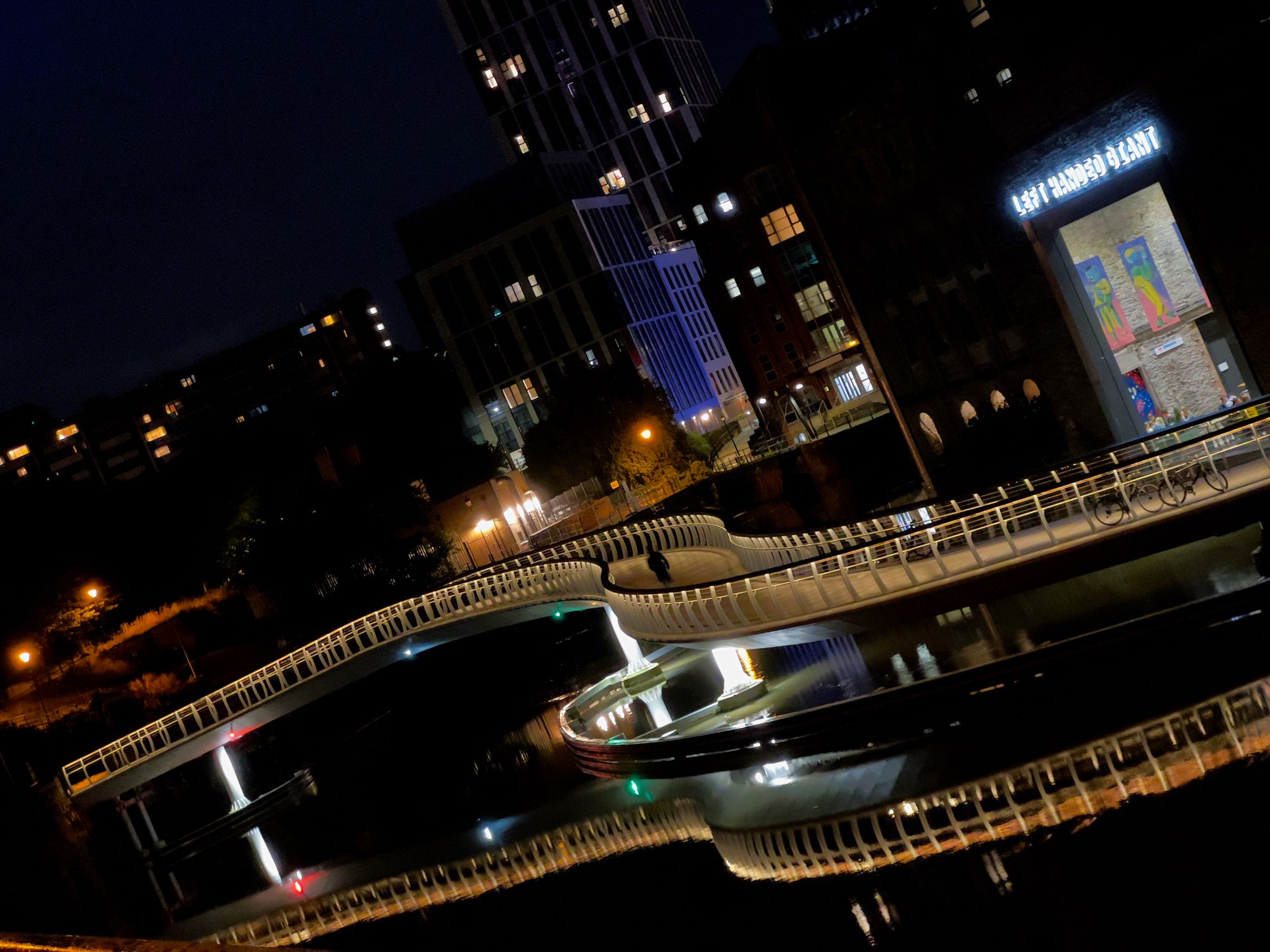 A twisty bridge over the river curves sinuously, reflected in the water. A lighted sign on the right bank reads "LEFT AHNDED GIANT."