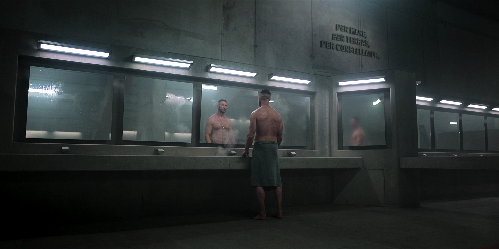 The Master Chief, wearing nothing but a dog-tag and a towel around his waist, stands in front of the mirror at a sink in a long row. Text set into the wall reads PER MARE, PER TERRAS, PER CONSTELLATUM.