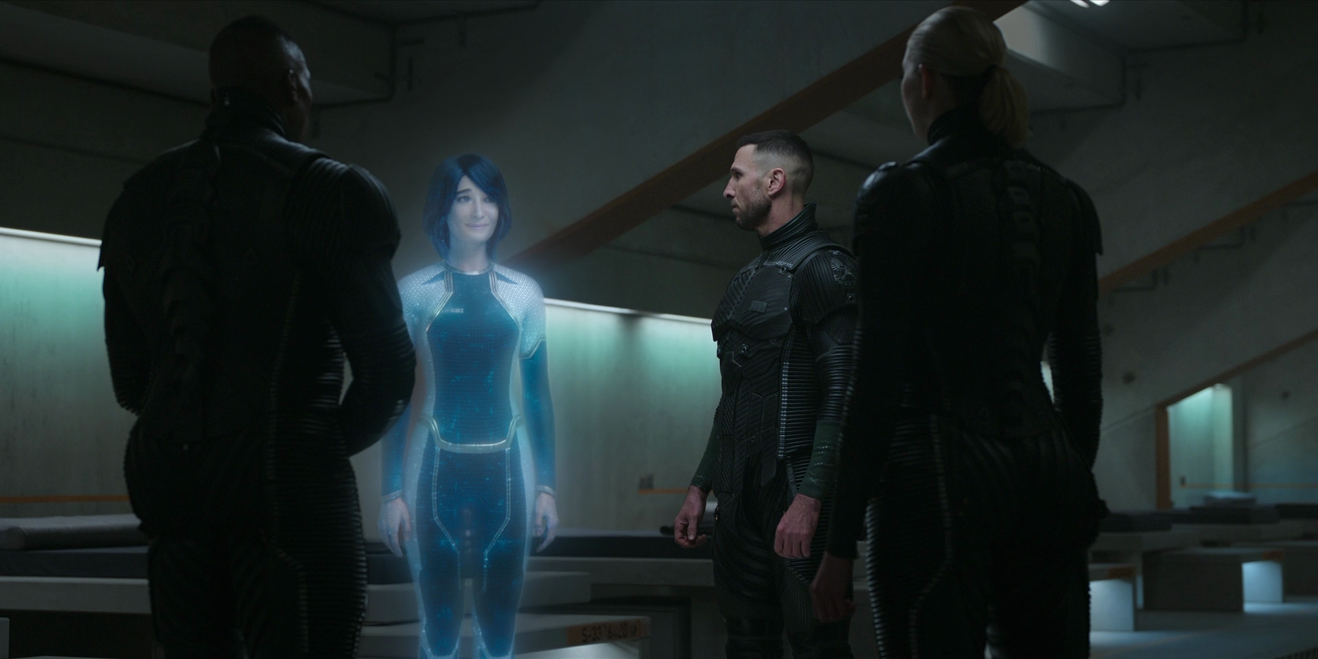 Cortana and the Master Chief stand next to each other with two other people around them. Cortana is smirking and looks embarrassed.
