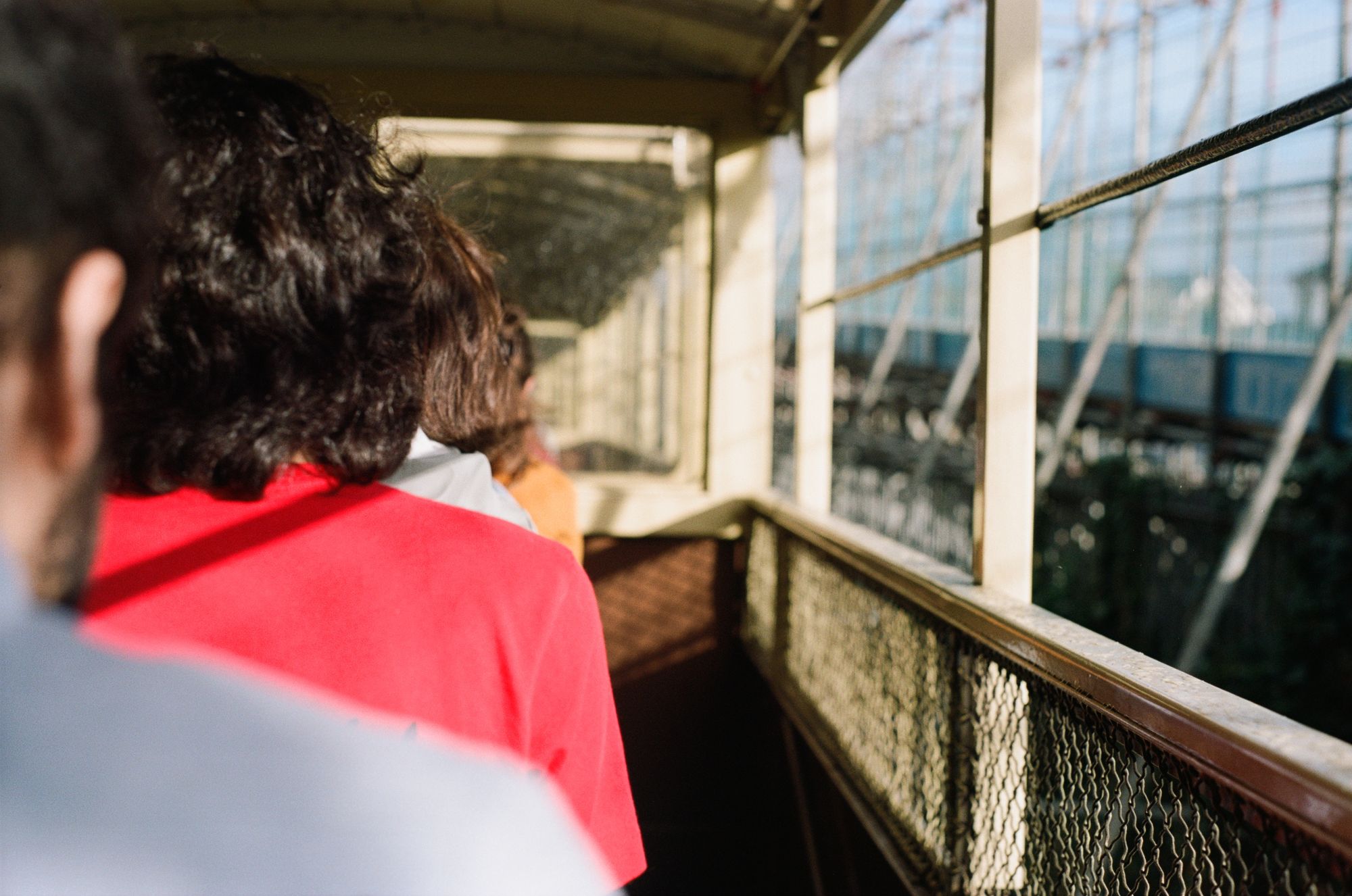 People seen from behind sit in an open railway carriage in golden light. The sun casts shadows across one man's red shirt.