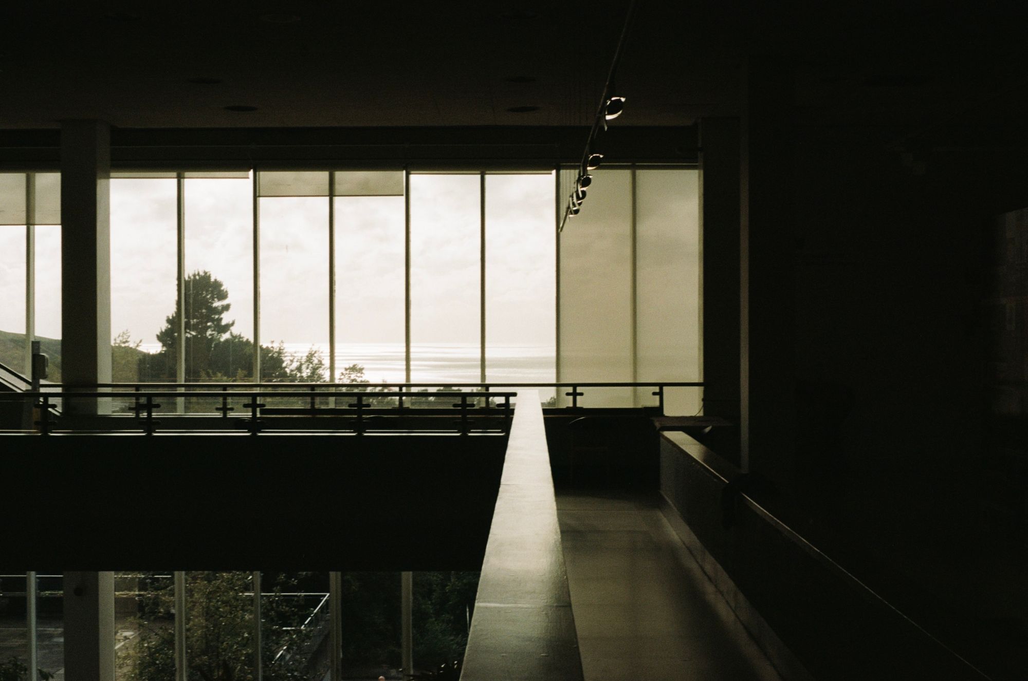 A mezzanine walkway in a large atrium with floor-to-ceiling windows looking out to sea on a grey day.