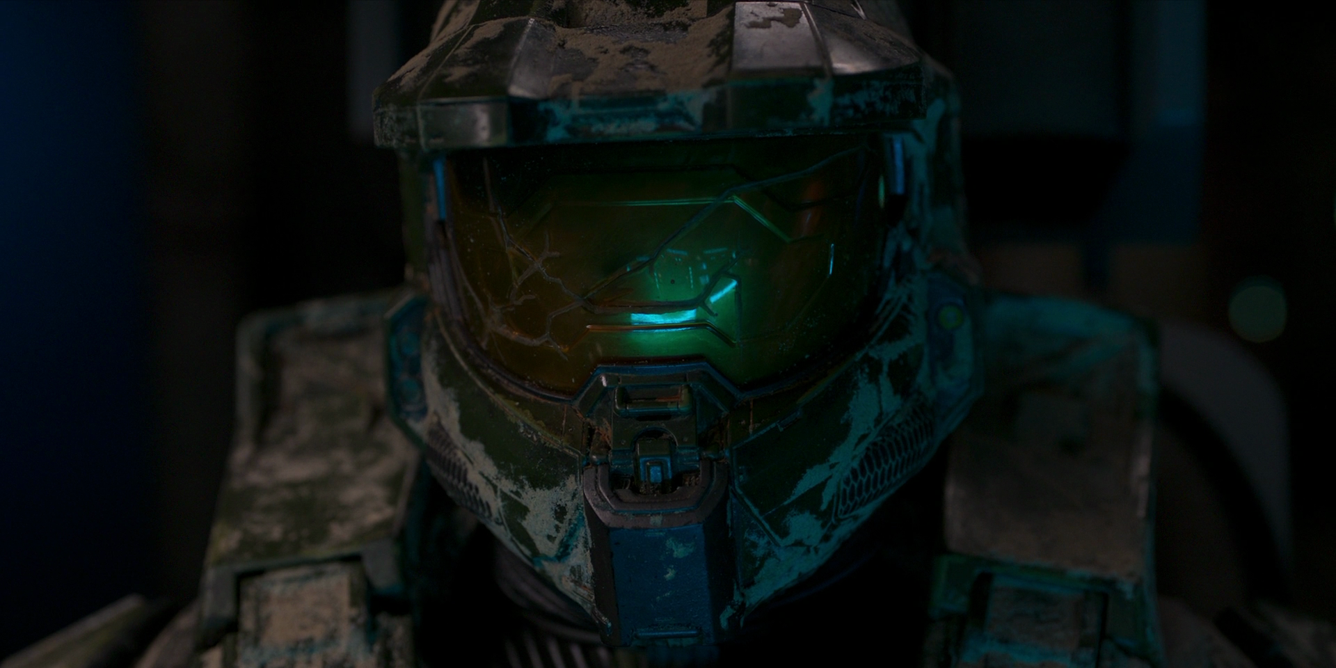Close up shot on the Master Chief's face with his helmet on, with a cracked visor and debris all over the chin piece, visor, and shoulders.