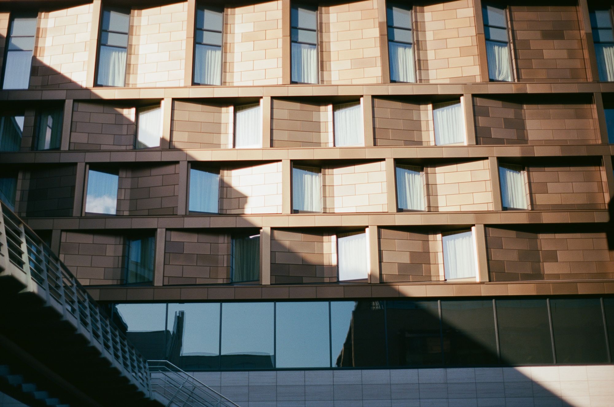 A wall of crenellated hotel rooms with brownish shiny metallic cladding, with a sharp shadow cast across it. A Medway runs off to the left.