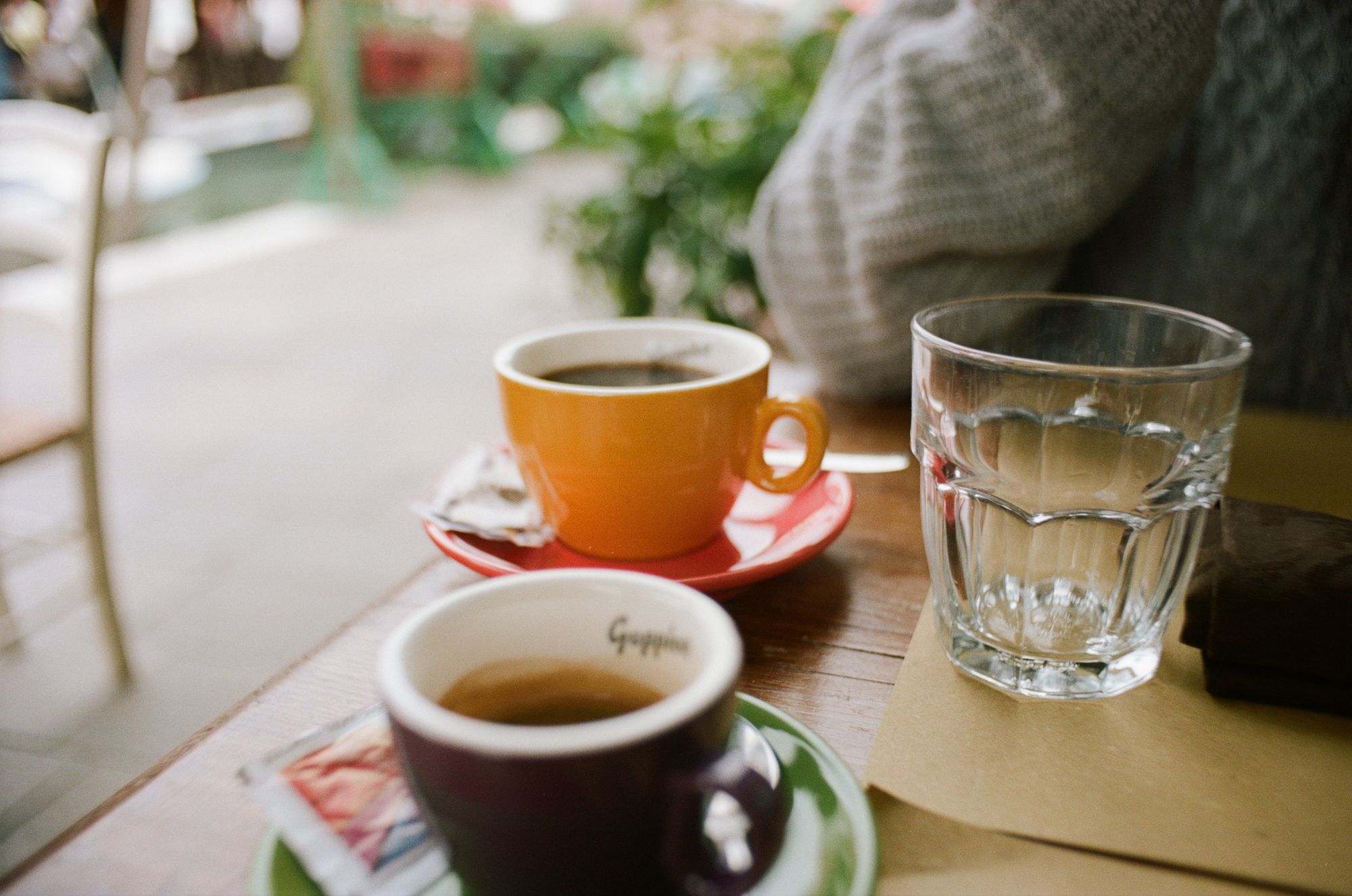 Two colourful coffee mugs on a table al fresco with a canal behind it.