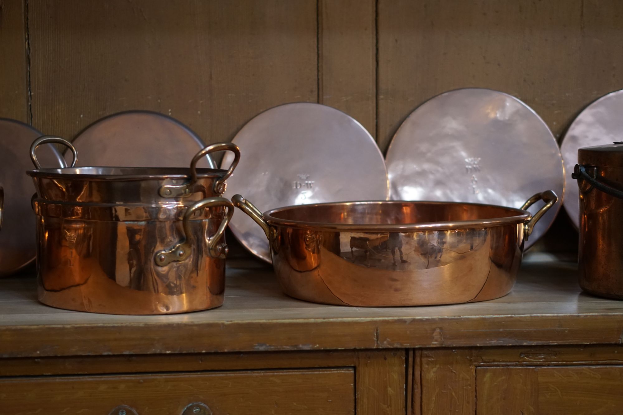 Copper pots and pans and silver platters on an old wooden sideboard.