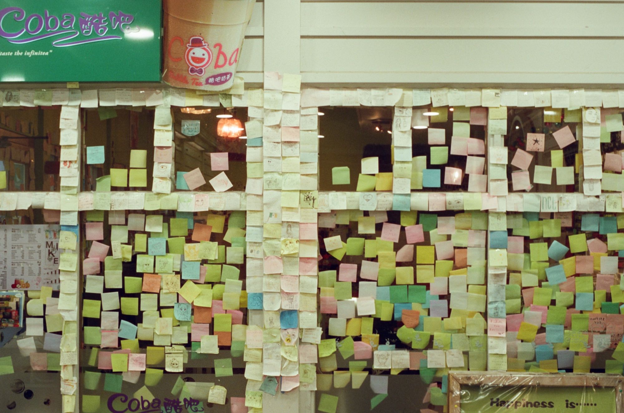 A boba tea shop called "Coba" with tons of colourful post-its from visitors stuck on the frames and glass of its windows.