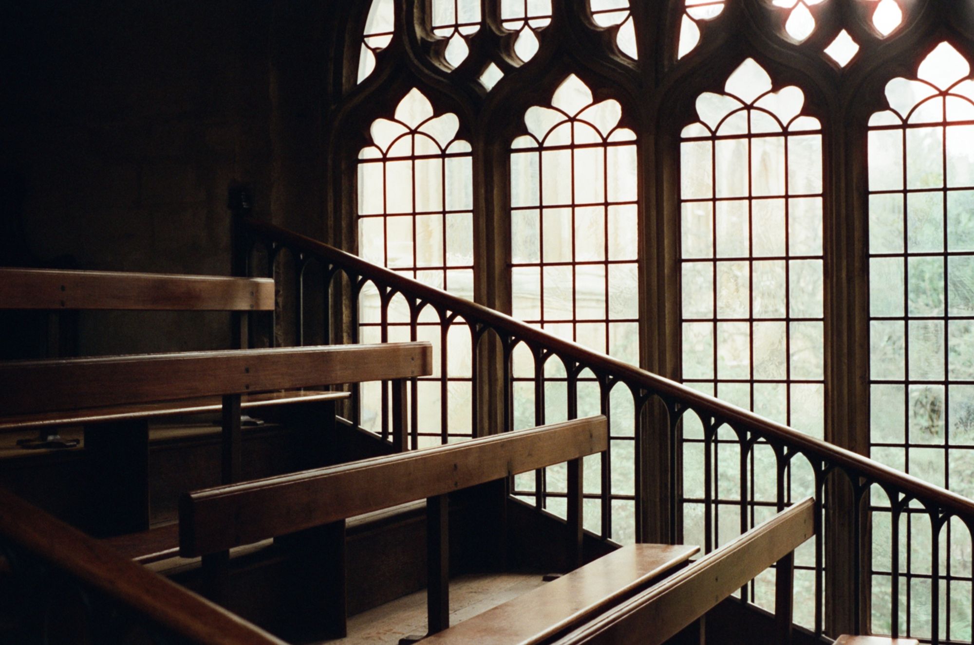 A row of wooden pews rising towards the back of a church, with sunlight coming through arched windows.