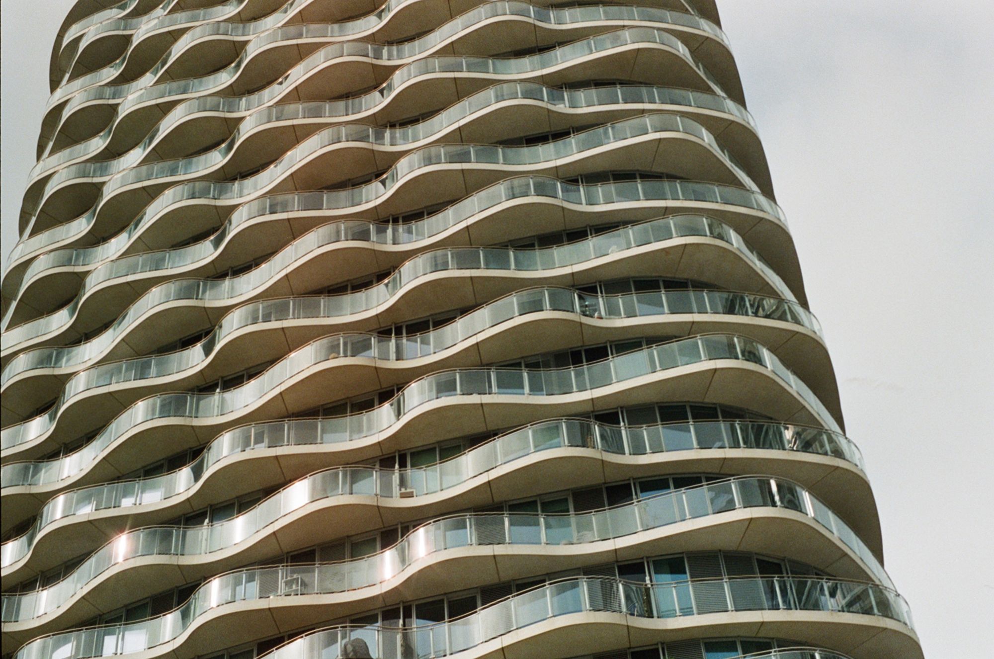 A tall apartment building with wavy glass balconies that form crenellations, each being different on different floors.