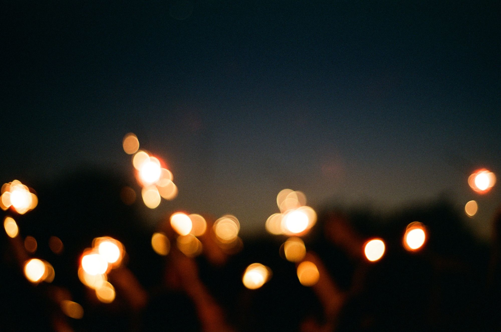 Defocused golden sparklers on a dark blue sky with some yellow remnants of sunlight on the horizon.