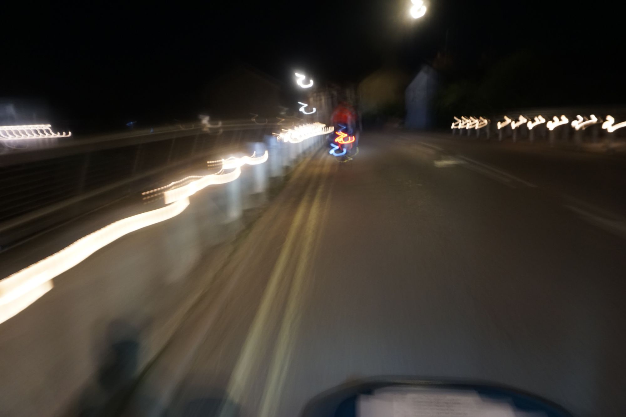 Blurry shot crossing a two-lane road bridge with lit bollards and modernist arced balustrades on either side.
