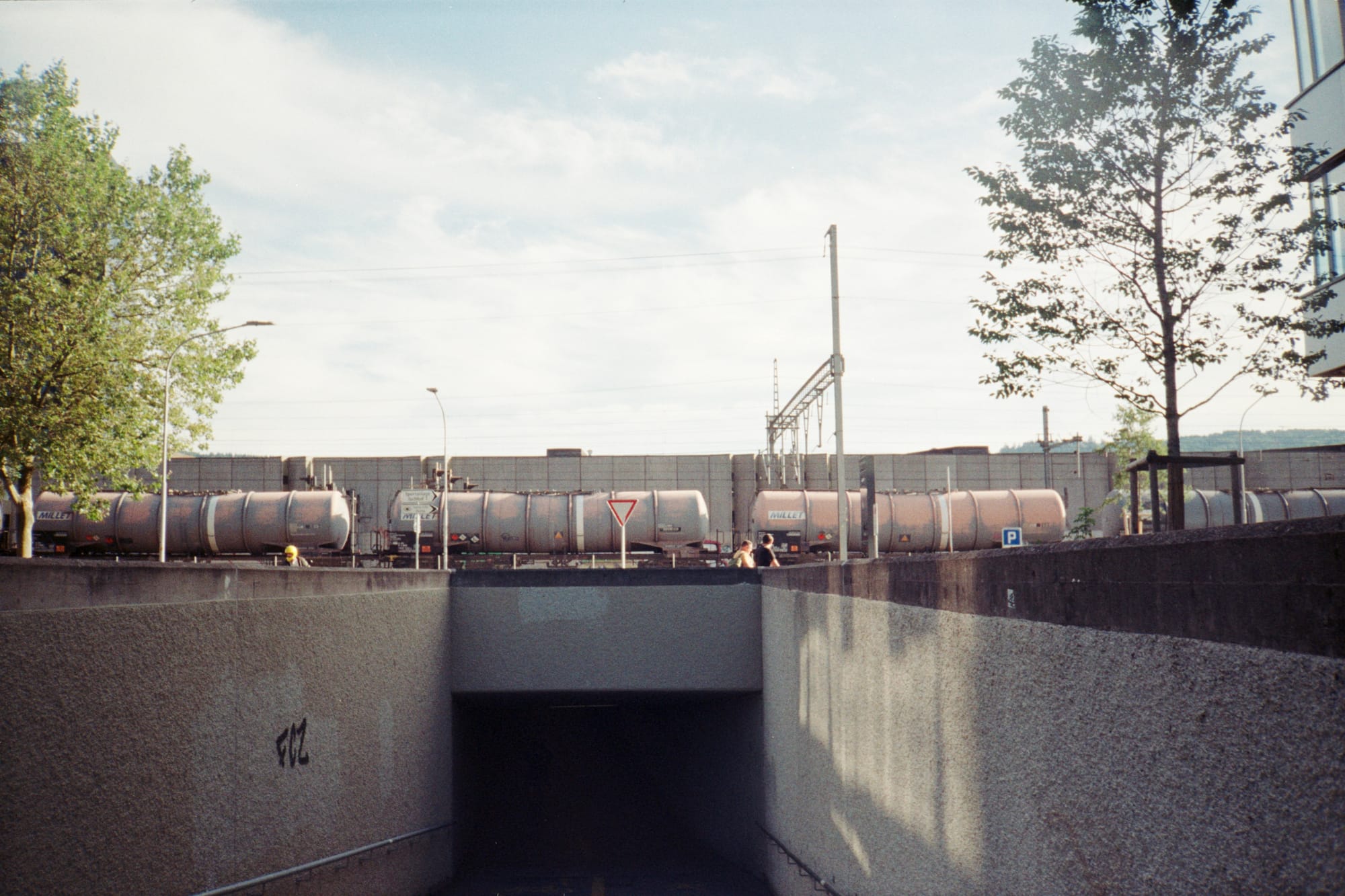 On a sweltering day, from the mouth of an invitingly dark and cool underpass, a tanker train rumbles over the top. We can see a Give Way sign for traffic joining the parallel road too.