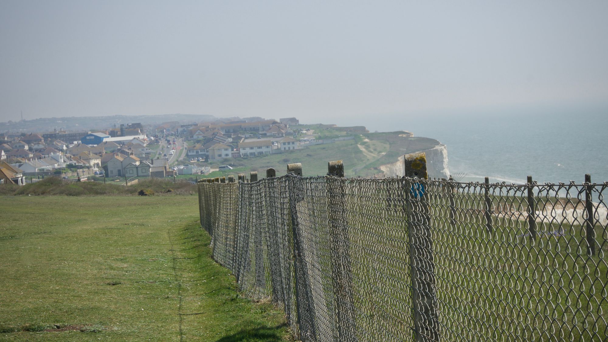 A cliff-edge with wire fencing looking east towards a town