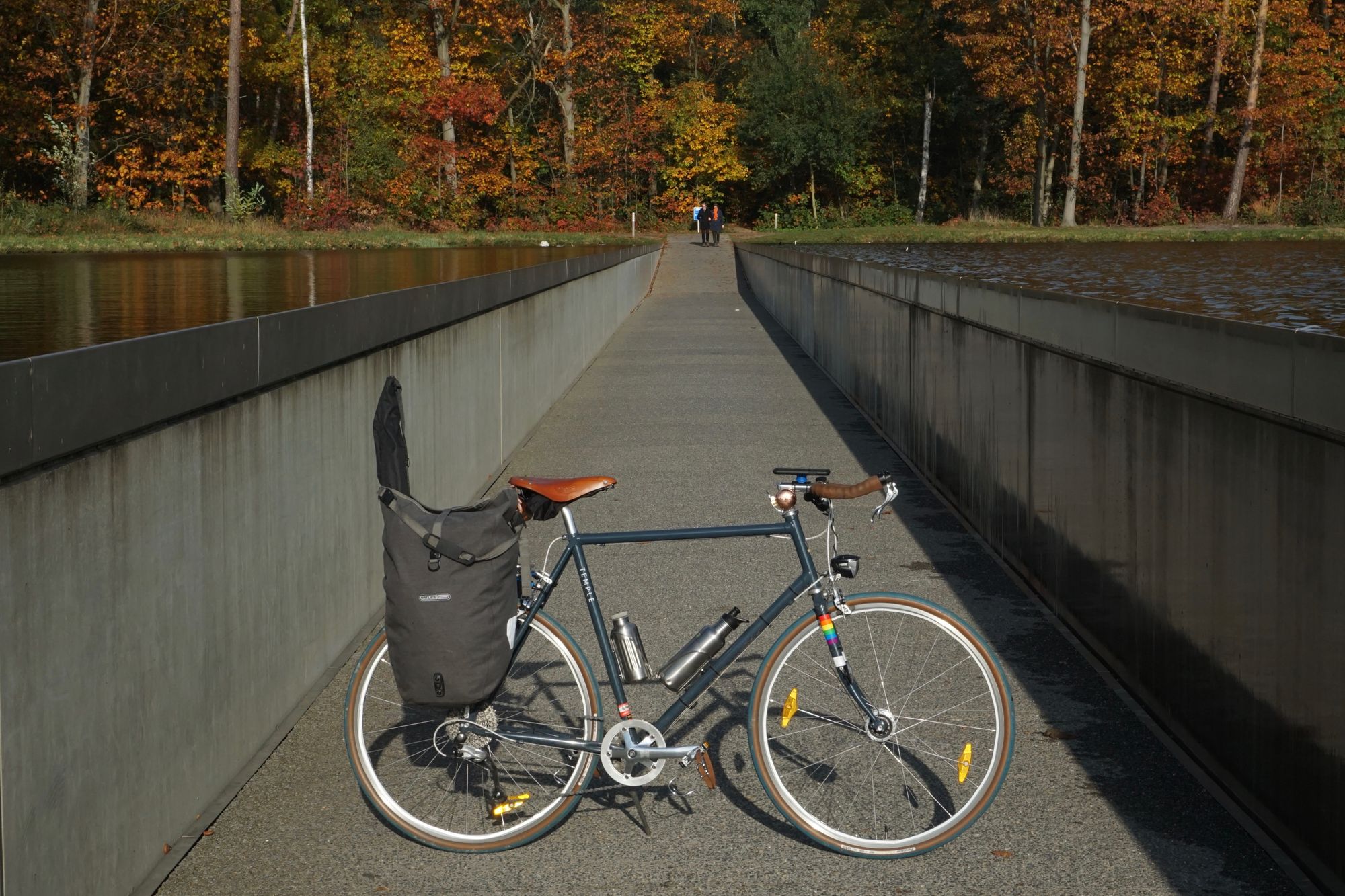 A loaded step-over bicycleon its kickstand on an asphalt path, in a cutting in an artificial lake.