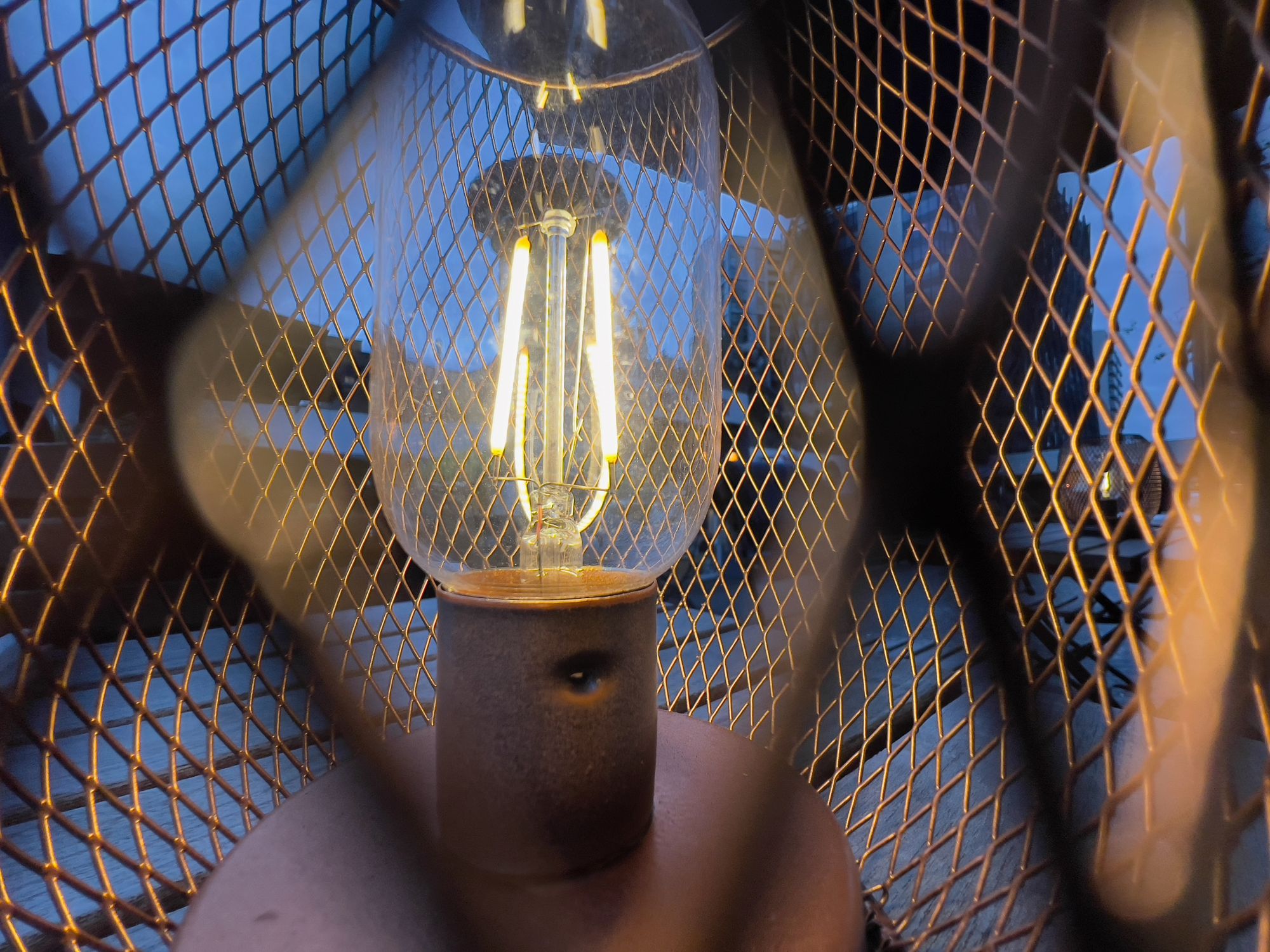 Close up on a small table lamp with a copper lattice circular design around a tall filament bulb in the centre.