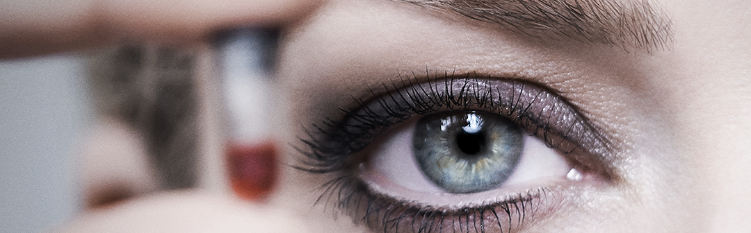 Close up on a woman's eye as she holds a tiny vial of blood up to camera.