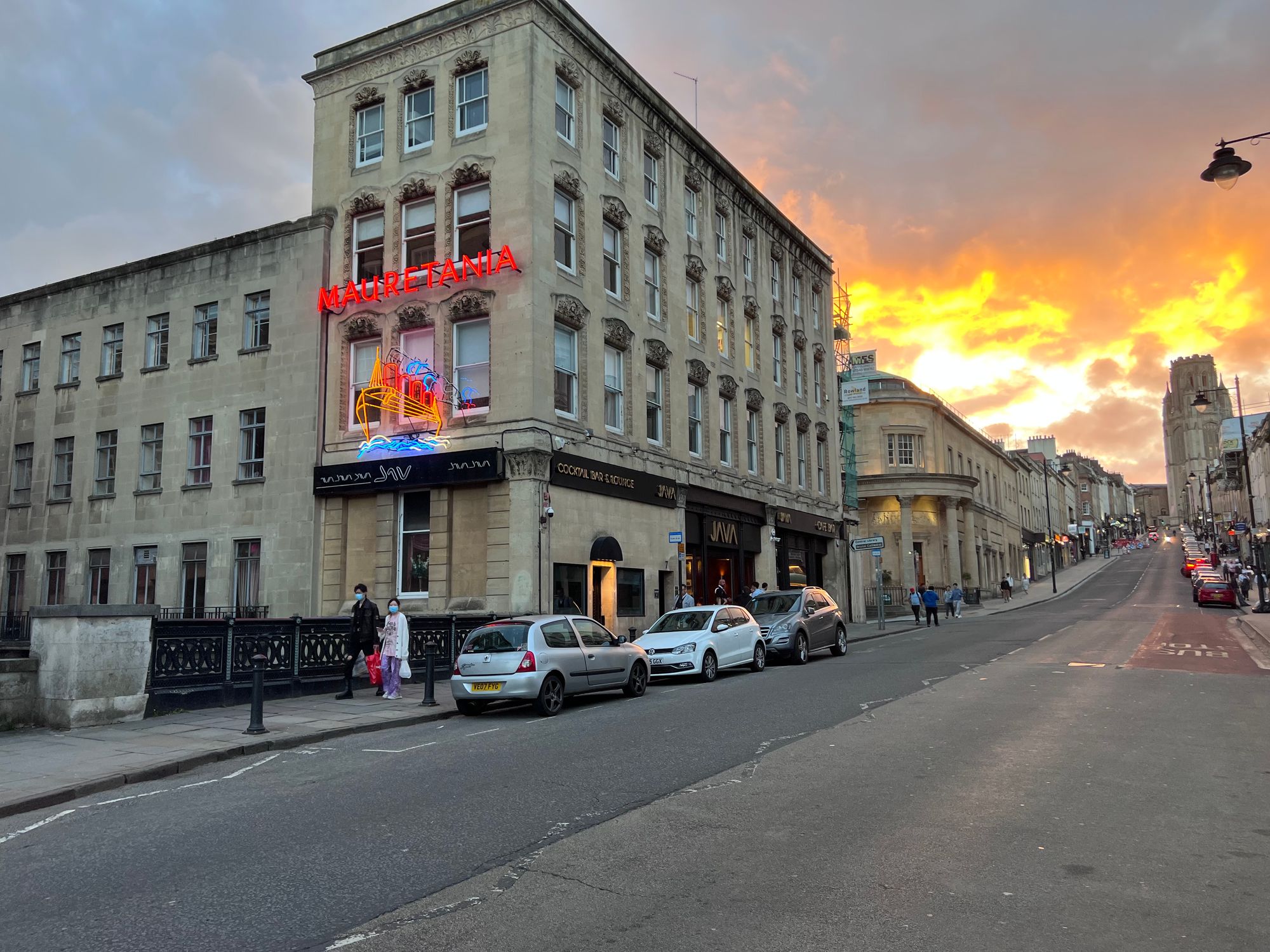 Looking up Park Street in Bristol towards a sunset. A neon sign with a picture of a ship reading "MAURETANIA" is lit up.
