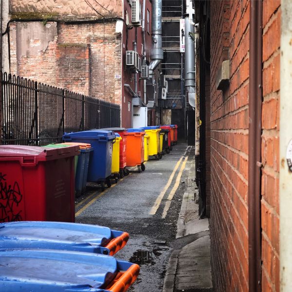 Row of multi-coloured plastic wheelie bins on a narrow street in Manchester