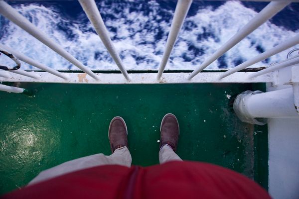 Looking down stood on the outside deck of a ship. The sea is visible past the railings.
