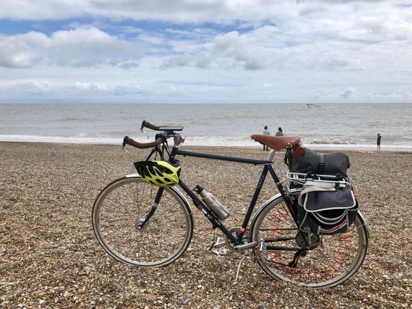 A step-over bicycle with panniers on the back, on its kickstand at a shingle beach.