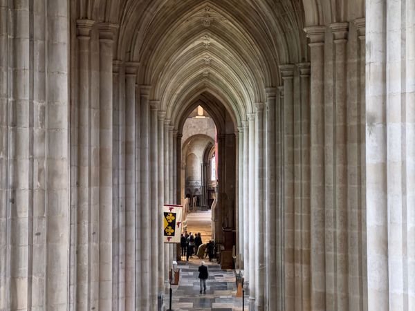 An arched aisle in Winchester Cathedral made of light-coloured stone, with a flag hanging partway along.