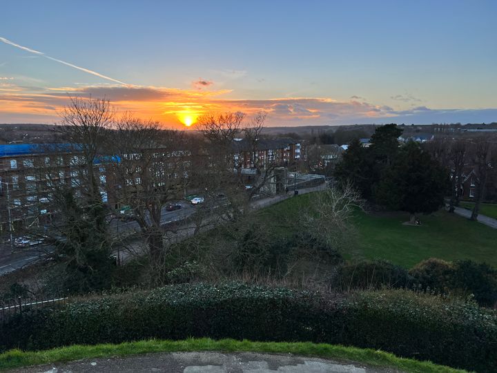 The sun sets as we look down from a hill over a green area and a large dual carriageway.