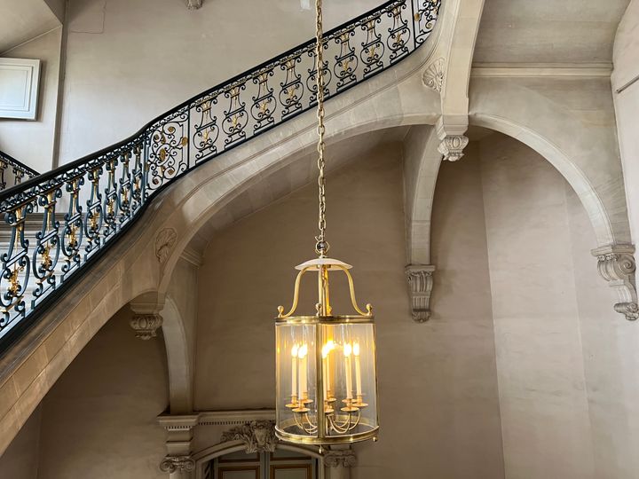 An ornate blue and gold staircase in a stone building with a glass jar chandelier, with candle-style lights inside.