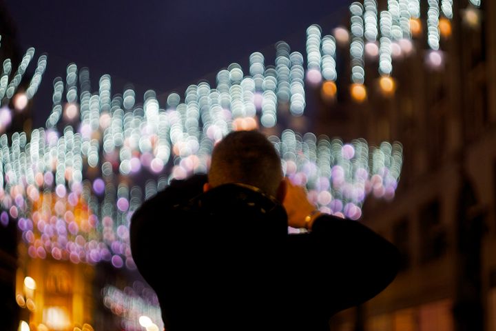 View from behind of a person taking a photo of Christmas lights on a phone. The lights are out of focus and swirl weirdly.