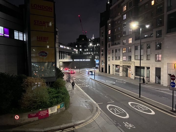 At night, a dual carriageway approaches a brutalist, round building, with an illuminated sign reading MUSEUM OF LONDON.